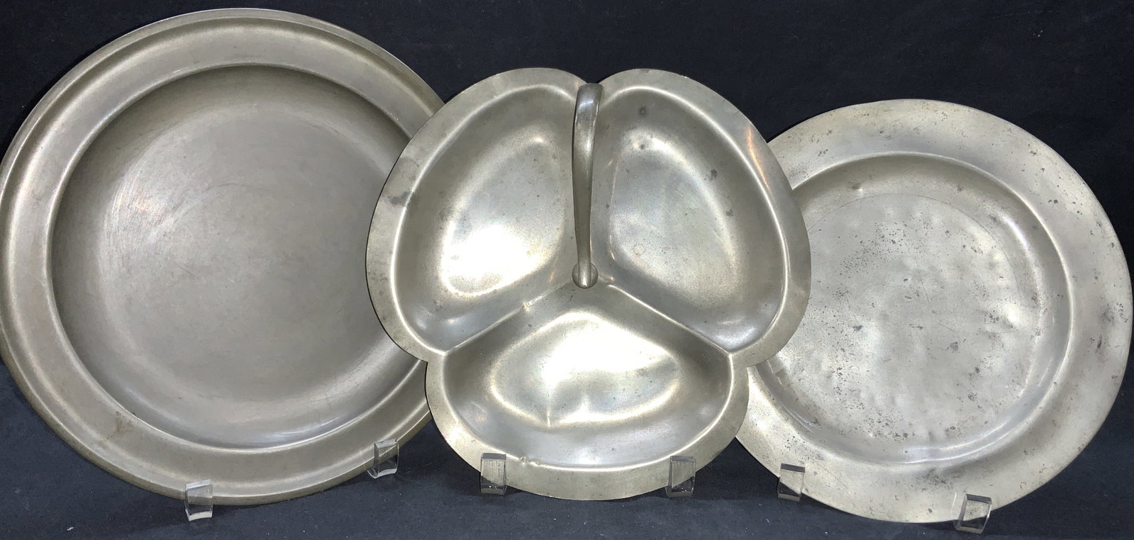 3 Pewter Made Dishwares Woodware & More: Lot of 3 pewter dishes, 1 sections into 3s and made to resemble a clover, approx 9.5 inch diameter. 1 dish marked C.A. Woodware, approx 10 inch diameter and one marked London. Approx 9 inch diameter. 