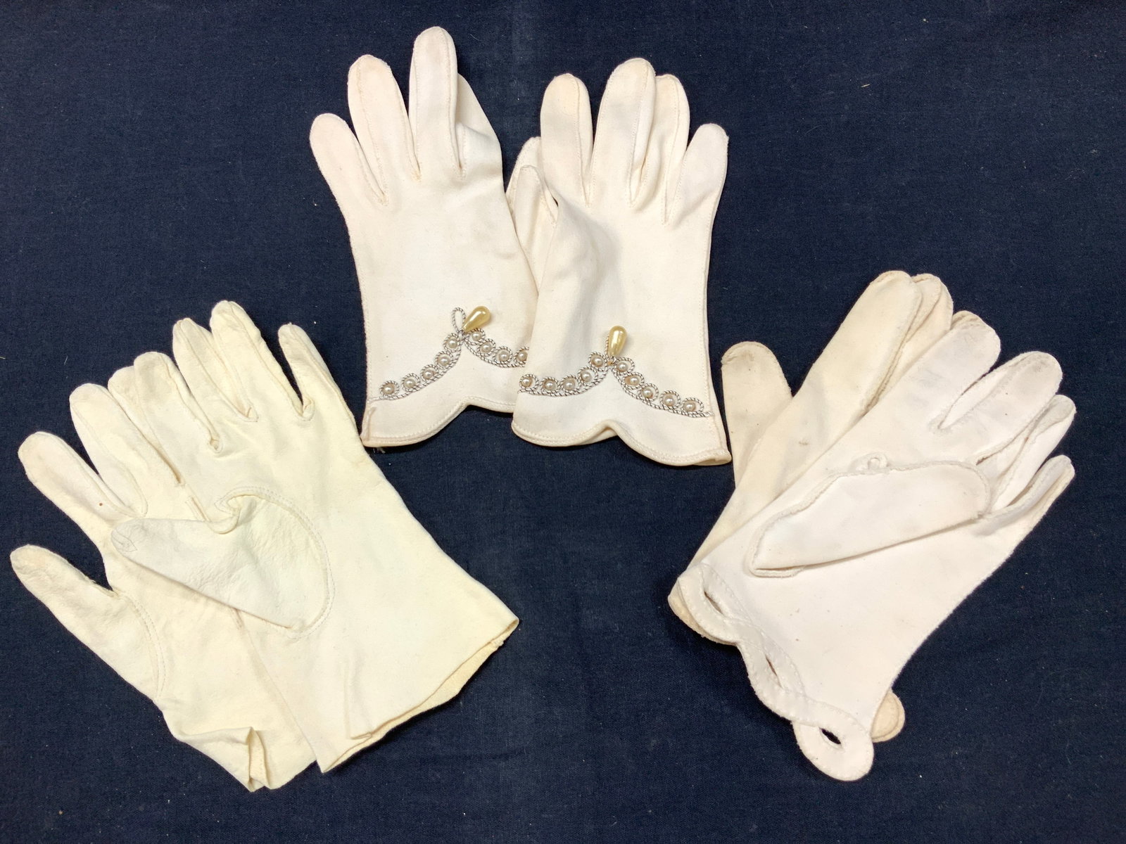 3 Pairs Vintage Cotton & Fabric Gloves: 3 pairs of vintage off white fabric gloves. Made possibly of cotton. 1 pair with three stitched lines on the tops, 1 pair with lopped wrist design and 1 pair with exterior pearlescent accents on wrist