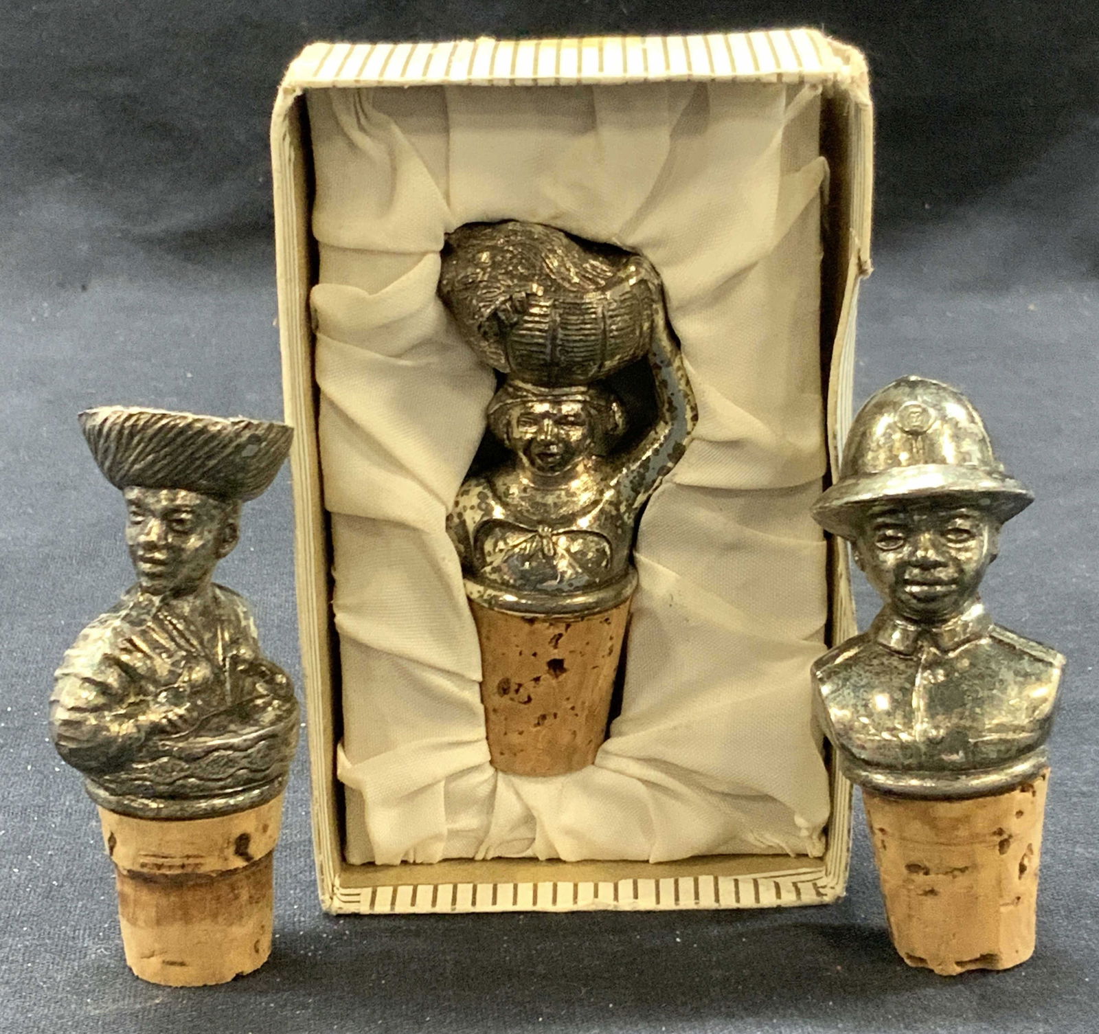 3 Vintage Silver Tnd Folk Art Bottle Corks: Lot of 3 vintage folk art bottle cork stoppers each cork with a silver toned figure, 1 depicting a police man, 1 man playing a drum and 1 woman holding a basket on her head. Comes in box 4 x 2.75 x 1.