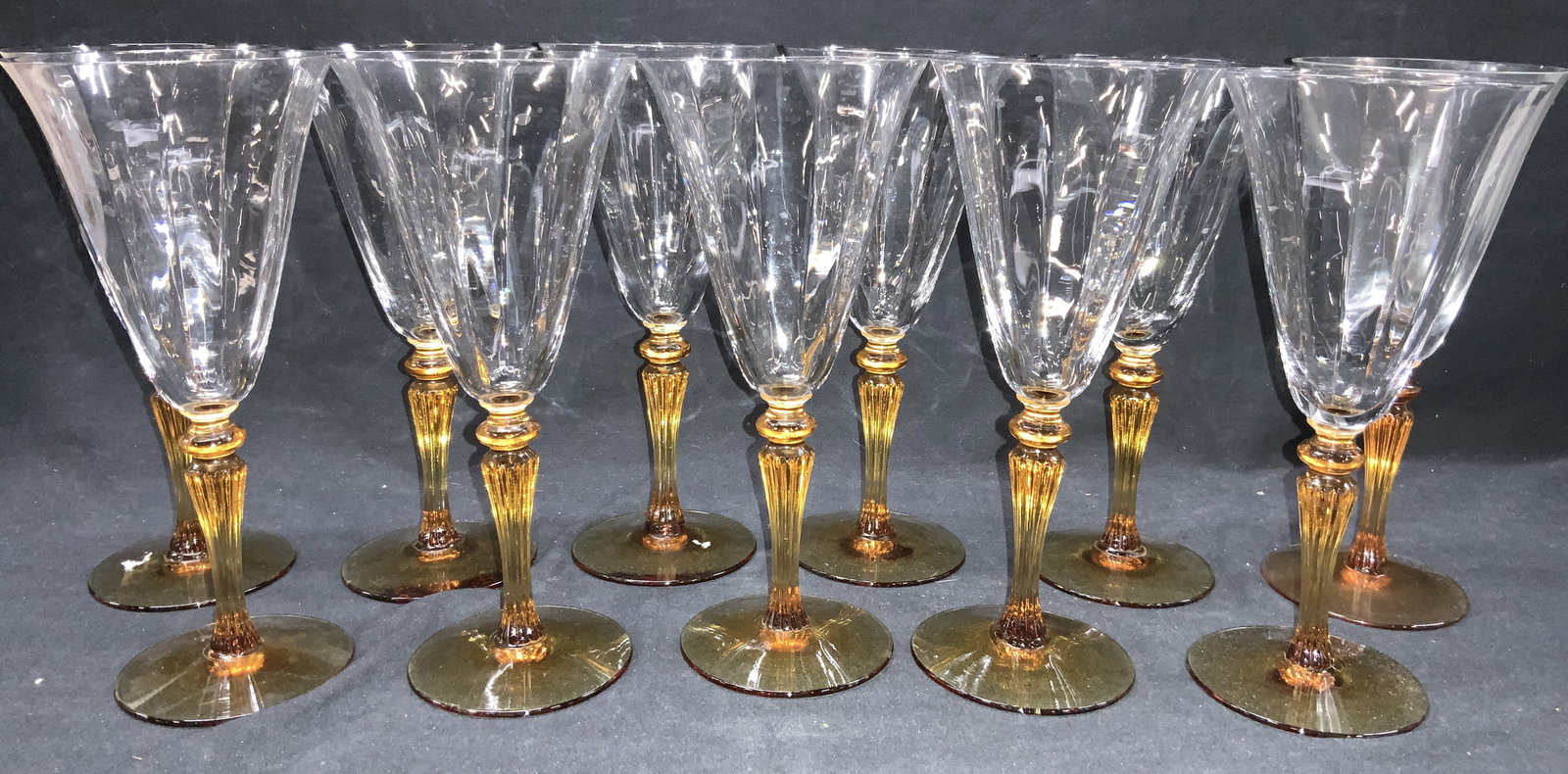 Set 11 Amber Glass Stemware: Set of 11 clear and amber toned stemware with amber toned stems. Approximately 8 inches tall and 3.75 inch diameter. Moderate cracking to clear glass cups. Amber glass stemware, stemware, colored glas