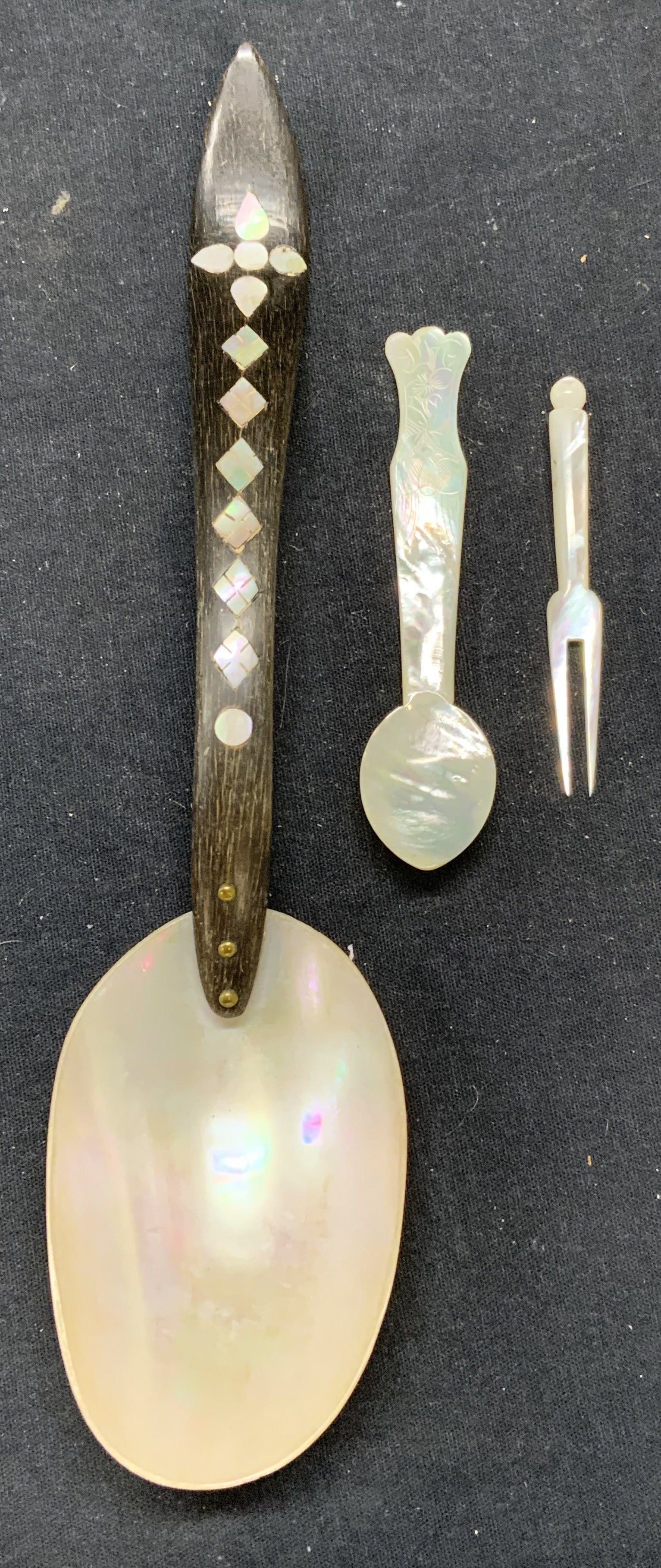Lot 3 Carved Mother of Pearl Flatware: Lot of 3 pieces. Mother of pearl spoon with wood and inlaid mother of Pearl handle. Mother of Pearl demitasse spoon with carved detail on handle. Mother of Pearl cocktail fork. All pieces have some su