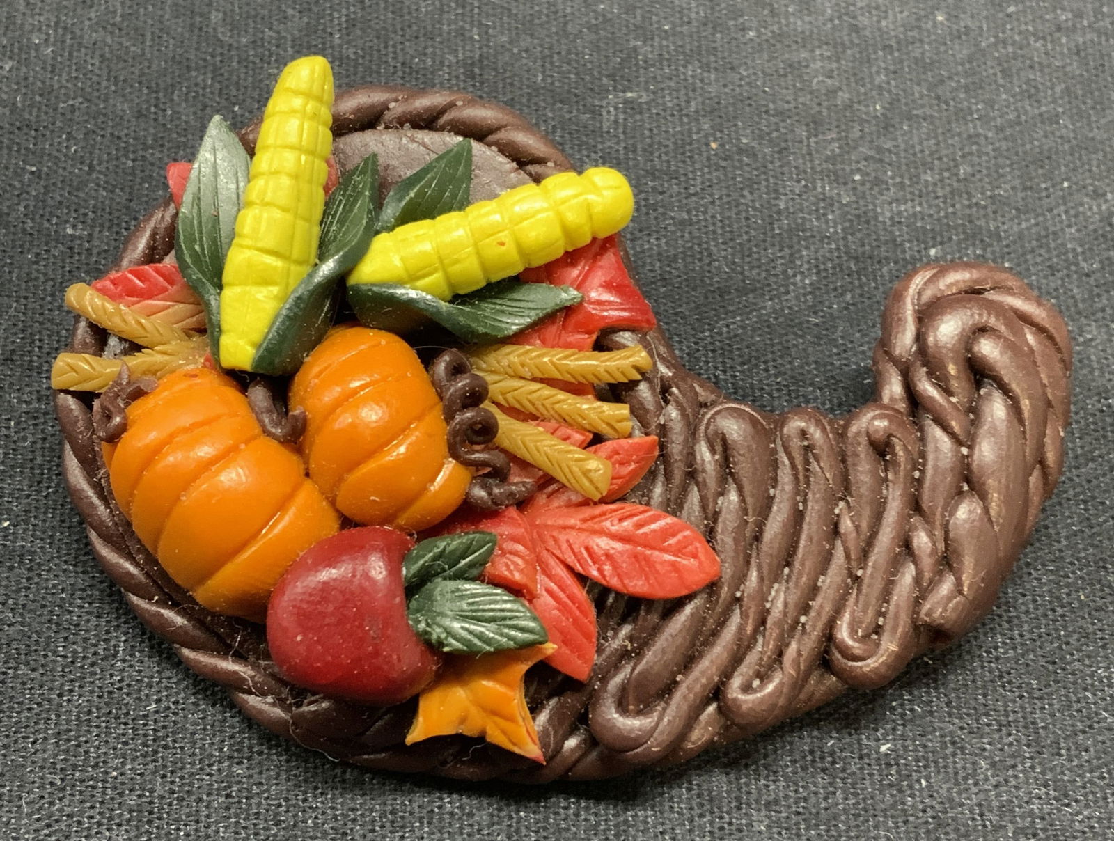 Handmade folk Art Cornucopia Brooch: Handmade folk art cornucopia with fall harvest vegetable motif. Material feels like clay. Hinge pin to underside. Some surface wear including scratched observed. Measures approx. 2.5 x 1.75 inches. Es