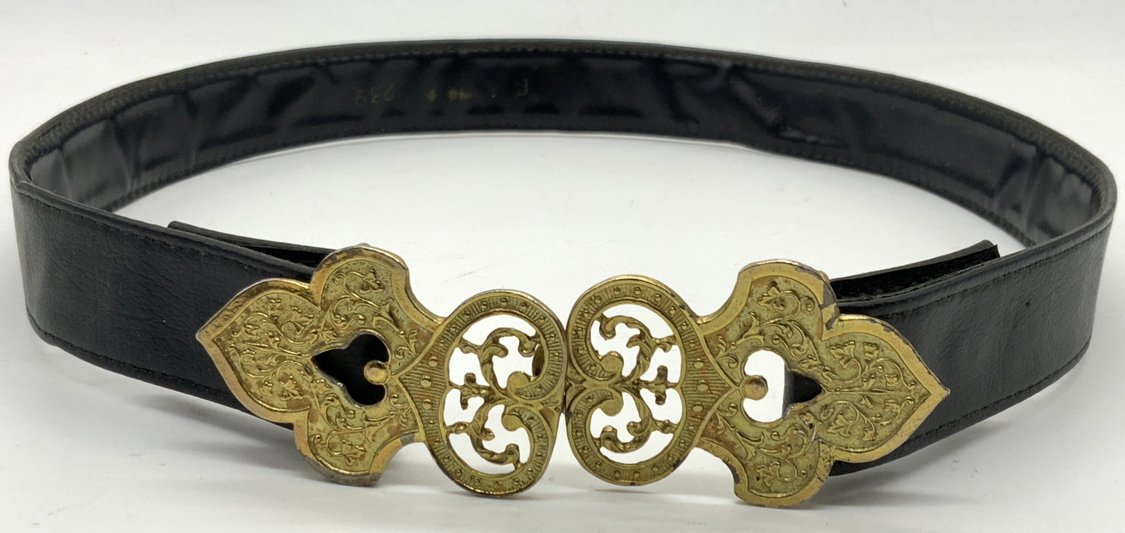 Black Leather Latch Fashion Belt: Black belt, possibly made of leather, with latch belt buckles made of white metal and coated in gold paint,. Buckle is ornately crafted. Approximately 27 inches long. Evident wearing to buckles and to