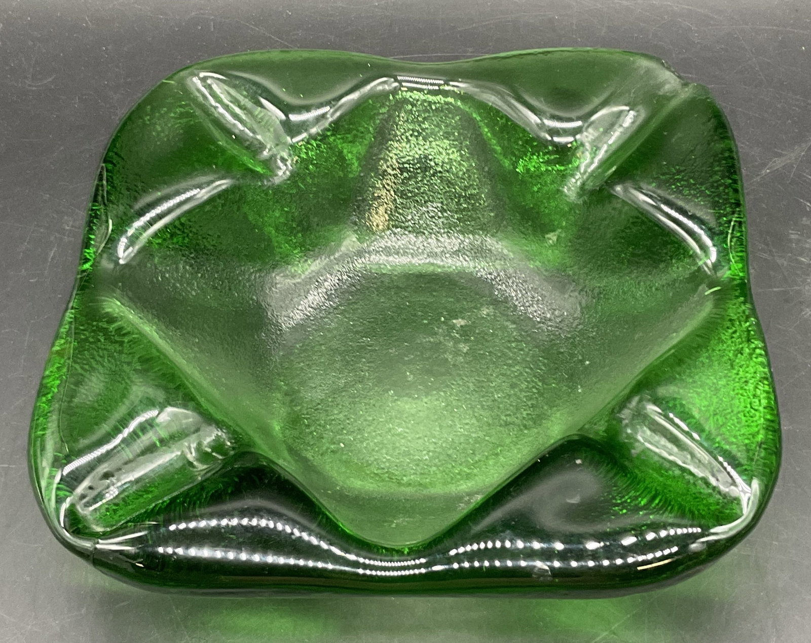 Vintage Green Glass Mid Century Style Ashtray: A thick walled and weighty vintage green glass mid century style ashtray. Textured and smooth glass. Measures approx 2 H x 7 W in. Some surface wear consistent with age and use. Some residue present t
