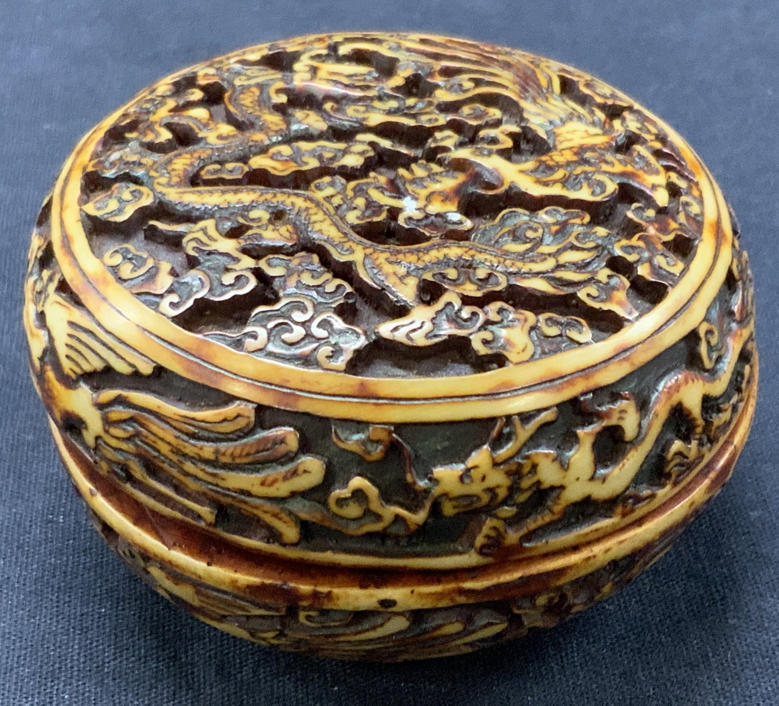 Carved Asian Dragon Trinket Box: Carved trinket box with Chinese dragon motifs with clouds throughout. Possibly carved resin or bone. Approximately 1.75 inches tall and 2.75 inch diameter. Moderate wearing to edges. Carved trinket bo