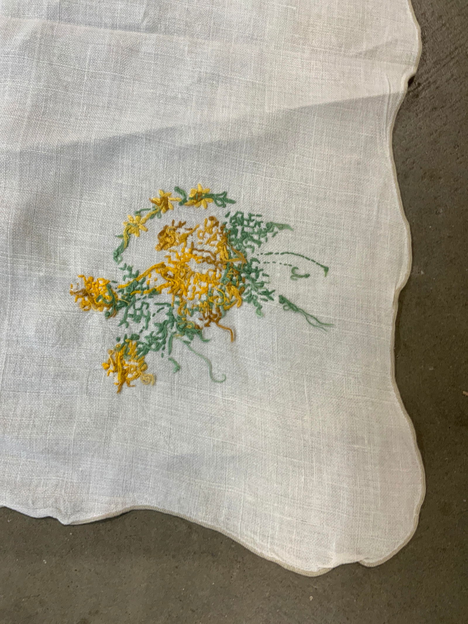 Vintage Embroidered Yellow Floral Tablecloth: A vintage cream toned linen tablecloth with scalloped edges. Yellow and green hued floral embroidery throughout. Measures approx. 48L x 48W in. Some discoloration and surface wear present. Linens, tex