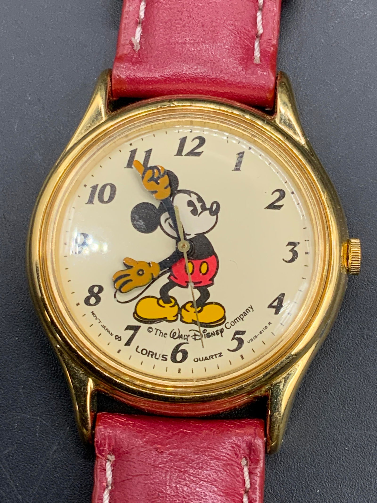 MICKEY MOUSE Walt Disney Company Leather Watch: A MICKEY MOUSE Walt Disney Company red leather watch featuring gold tone metal hardware. Watch face features Mickey Mouse. Reverse of band reads Genuine Leather, reverse of watch reads water resistant