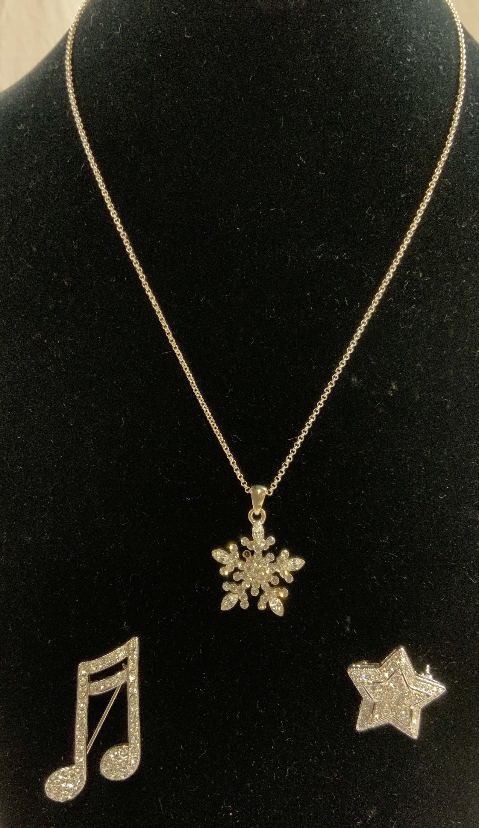 3 Rhinestone Brooches & Snowflake Pendant Necklace: Lot includes music note brooch, Star brooch, & Snowflake Pendant Necklace. Each piece has rhinestone detail. Necklace has chain link and clasp. Necklace has at most 7 inch drop. Necklace, pendant neck