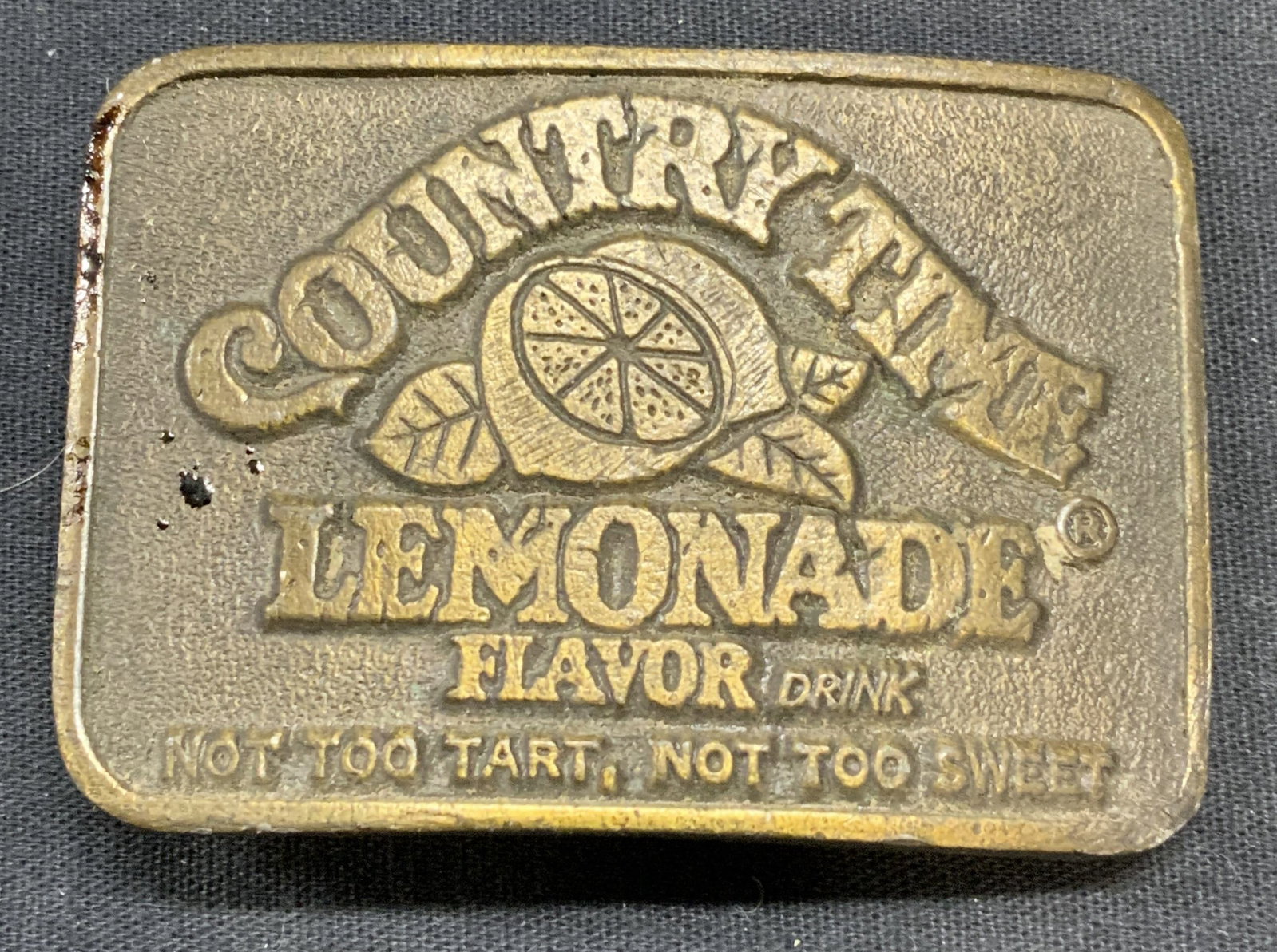Vintage Country Time Lemonade Belt Buckle: Vintage Country Time Lemonade belt buckle. Brass tone metal. Piece has weight. Measures approx. 2.75 x 1 7/8 inches. Surface wear including scratching and patina observed. Belt buckle, metal belt buck