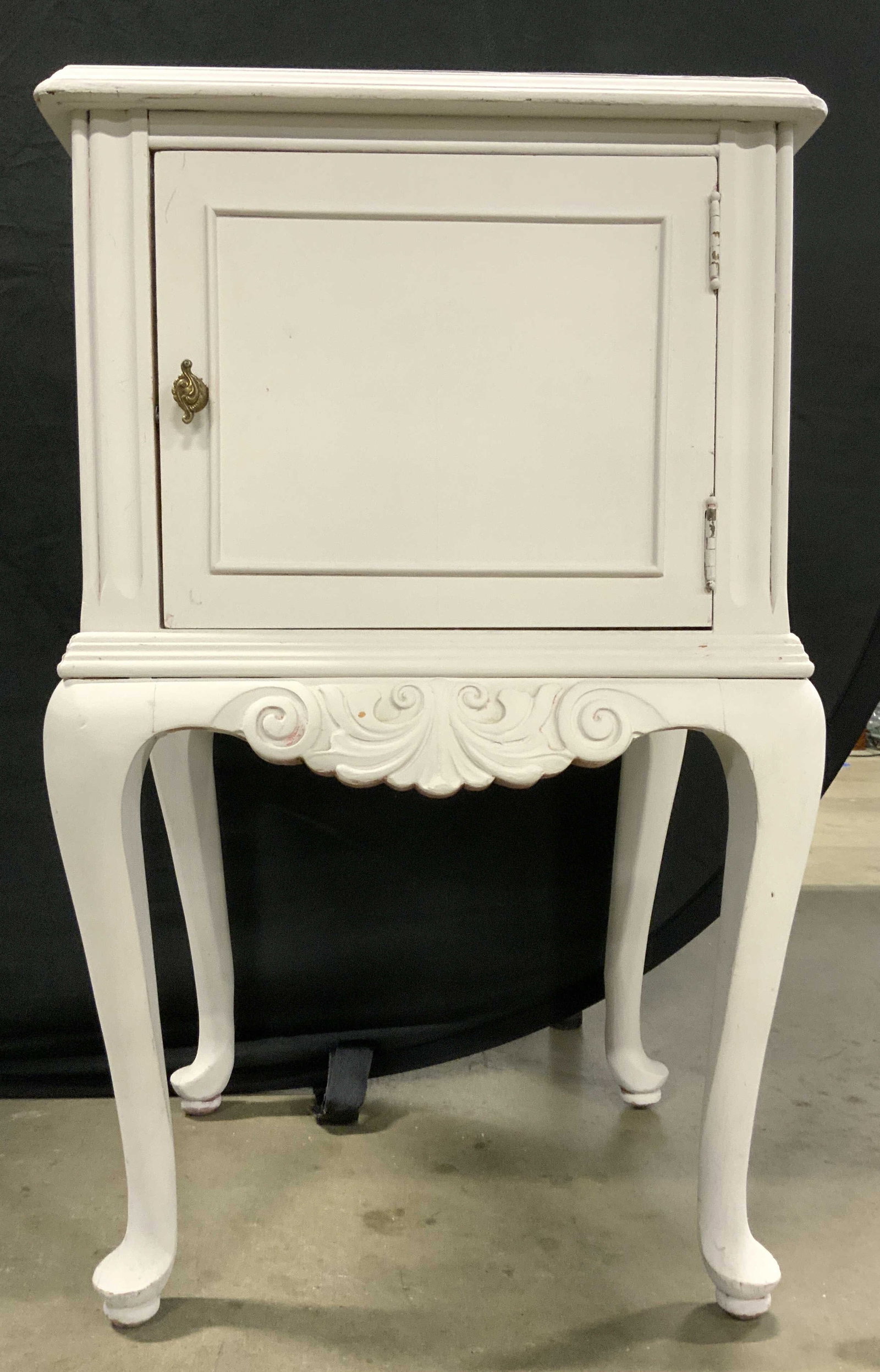 Queen Anne Vintage Wooden Nightstand: Nightstand is vintage and wooden. Piece is light slate toned with Queen Anne legs. Piece has carved scroll detail underneath cabinet door. Handle is gold toned appears to be brass. Nightstand measures