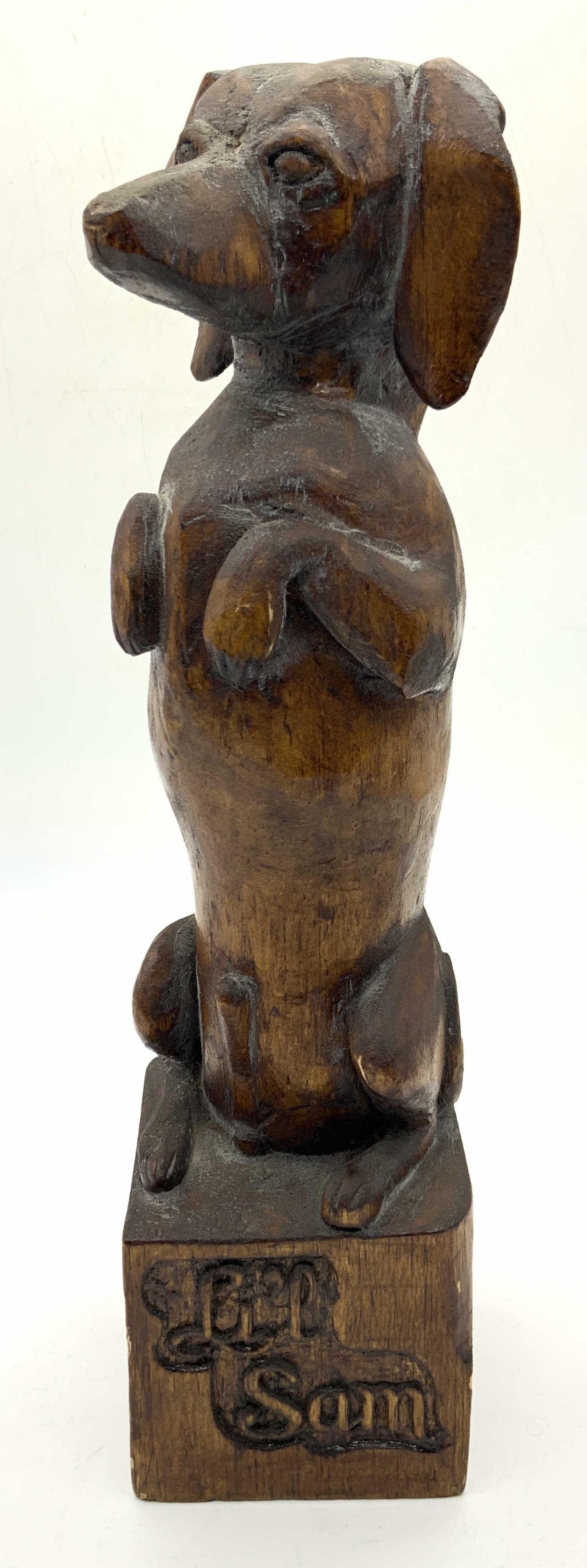 Lil Sam Carved Wooden Dachshund Figure: Carved wooden sculpture of a begging dachshund, standing on his hind legs, on a base that reads Lil Sam. Approximately 12 inches tall with base being 3 x 3 inches wide. Moderate wearing to wood throug