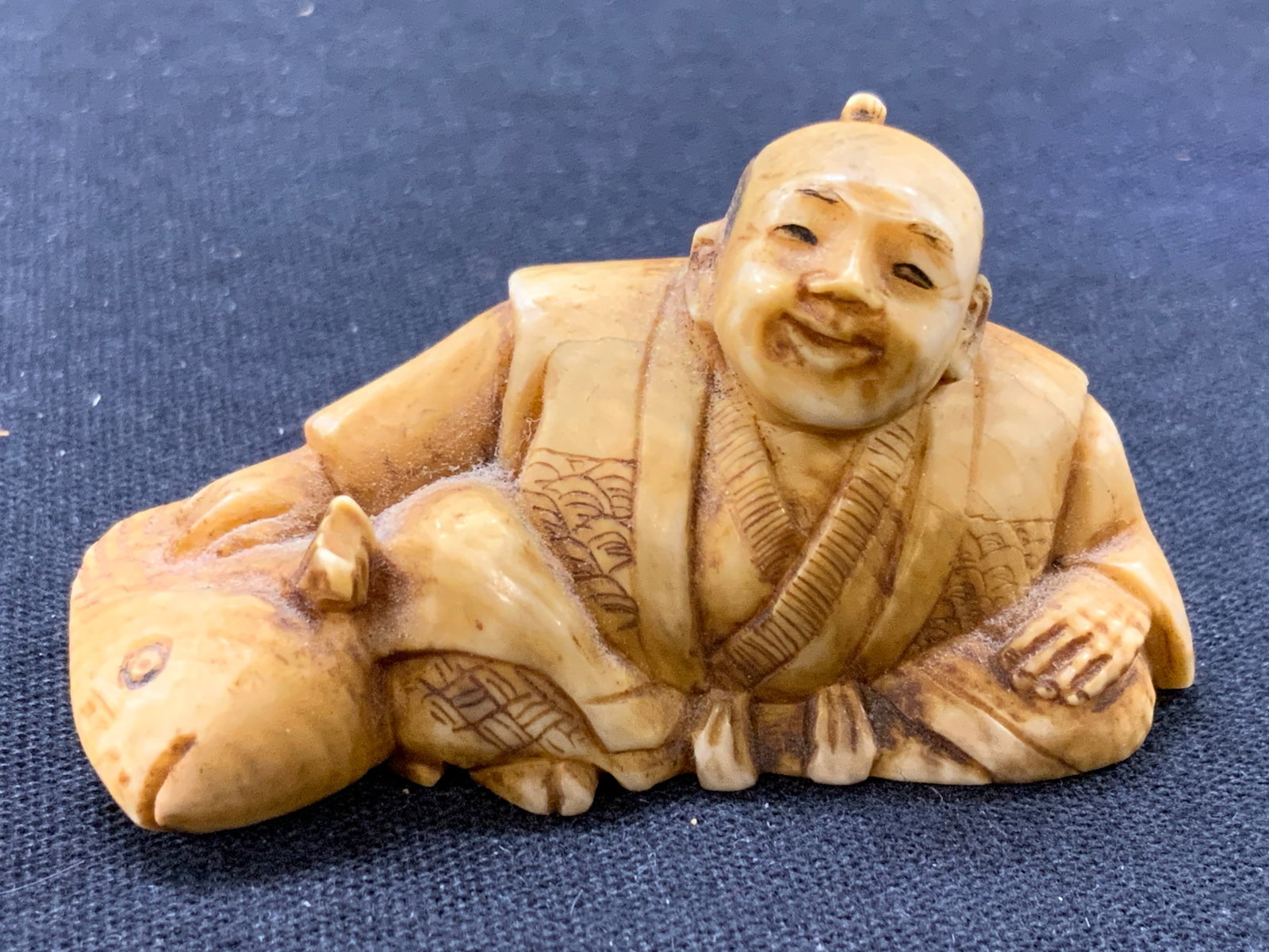 Japanese Carved Bone Man W Fish Netsuke: Signed on underside with Japanese hiragana. Netsuke depicts a man seated with a top knot hair in haori robes with a large fish next to him. approximately 1 inch tall and 2 inches wide. Moderate wearin
