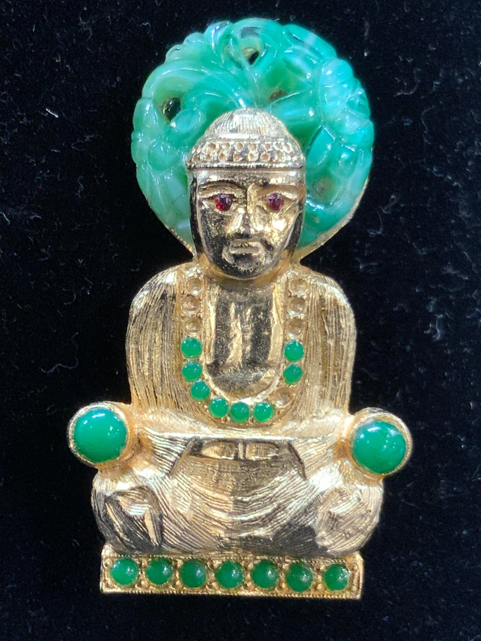 HATTIE CARNEGIE Stamped Gold Tn Buddha Brooch: Stamped on backside Hattie Carnegie. Gold toned metal Buddha brooch with jade green toned Cabochons and carved green toned glass halo behind the Buddhas head. Approximately 2 inches long and 1 inch wi