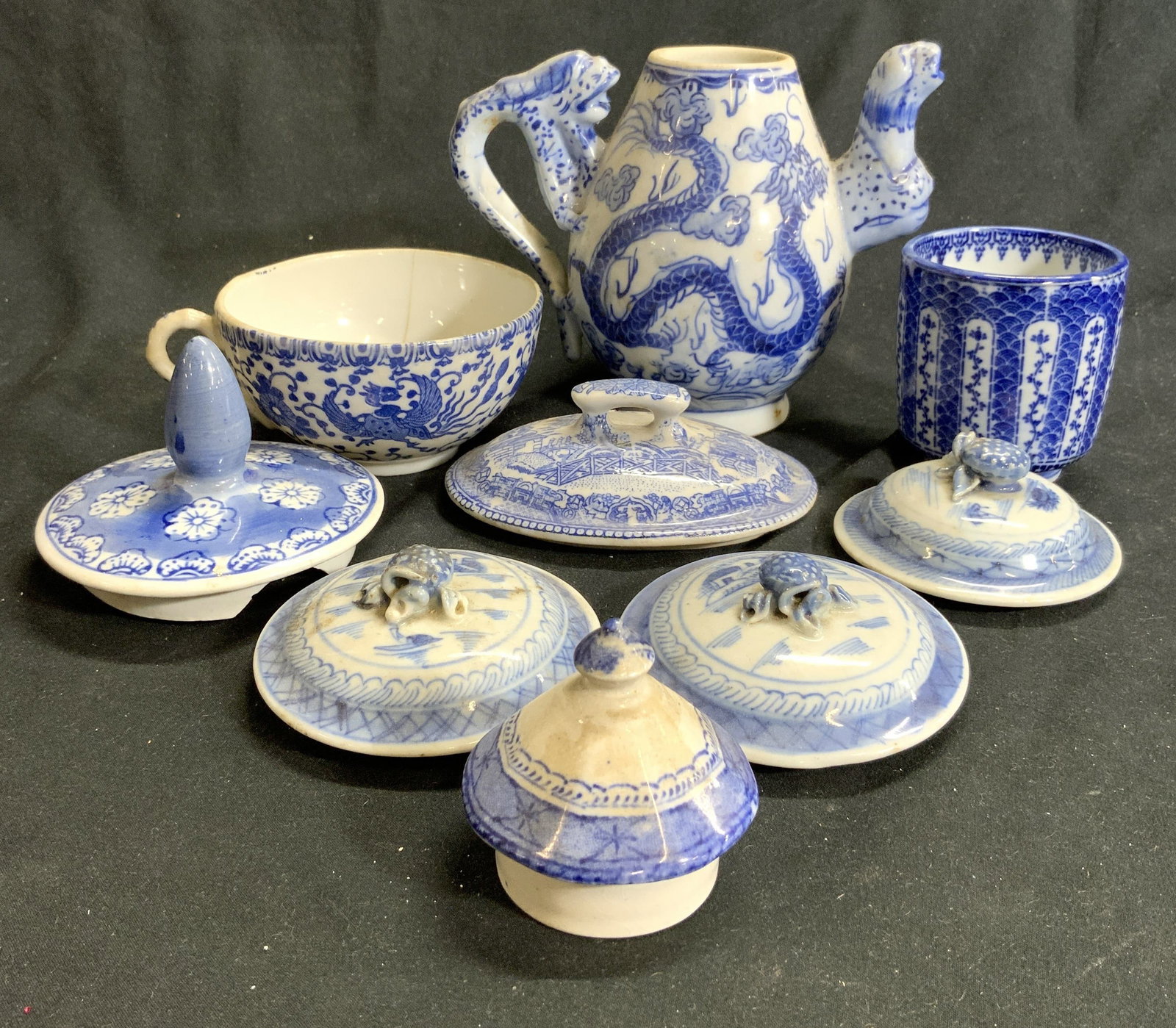 Lot 9 Vintage Blue Willow Porcelain: Lot includes 6 lids, 1 teacup, 1 teapot, & 1 vessel. Pieces are all white with each with different blue toned detail. Teapot measures approximately 5 inches tall 3.5 inches wide 6 inches deep. Porcela