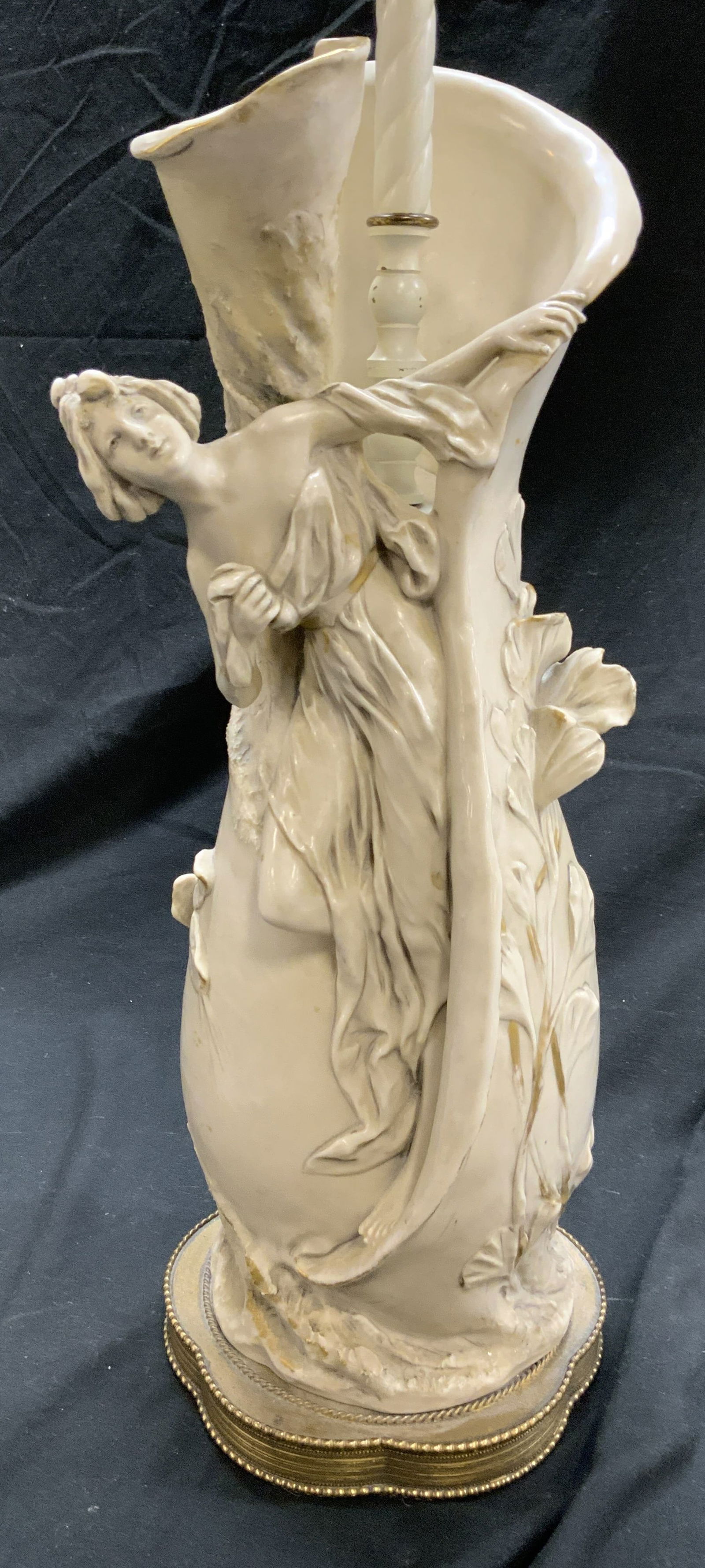 Vintage Female Figure Porcelain Table Lamp: Lamp is vintage and porcelain. Piece depicts a female figure wearing draped cloth. Lamp has floral & leaf detail. Base is gilt metal with beaded edges. Lamp includes wooden finial. Piece measures appr