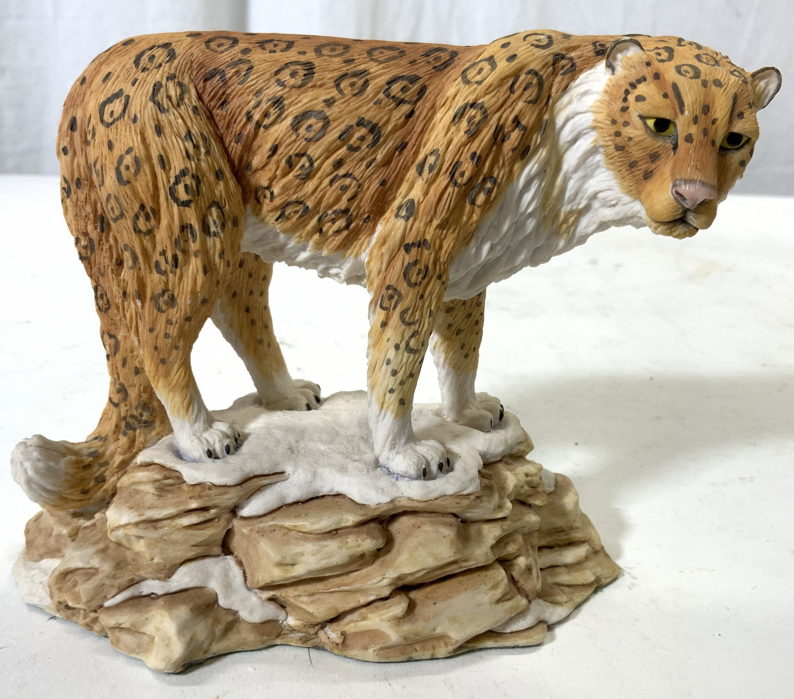 Bisque Leopard Figure Felt Underside: Piece depicts a leopard figure standing on a snow covered boulder. Figure appears to be vintage and bisque. Underside is green toned lined with felt. Piece measures approximately 5 inches tall 6 inche