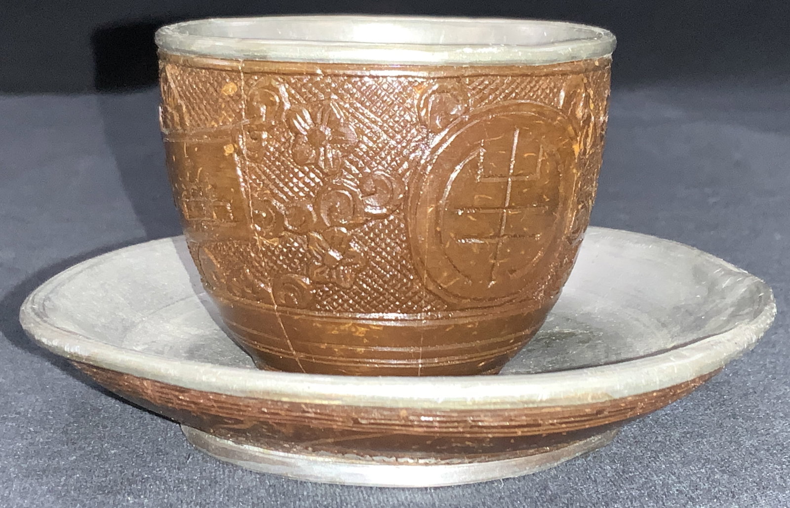 VNTG Asian Style Carved Wood & Pewter Cup & Dish: Vintage set of a cup and saucer with exterior being made of carved wood, possibly resin on both the cup and saucer. Motifs of lucky Chinese symbols and florals with pewter center and interiors. Cup is