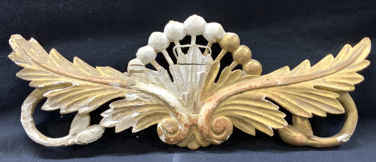 Carved Wooden Gilt Winged Wall Trim: Carved wooden and plaster made wall ornament, trim. Gold leafed. Has wings with scroll motifs. Evident loss to gilt on wings and cracking to wood. Approx 7.5 inches tall and 19 inches long from wing t