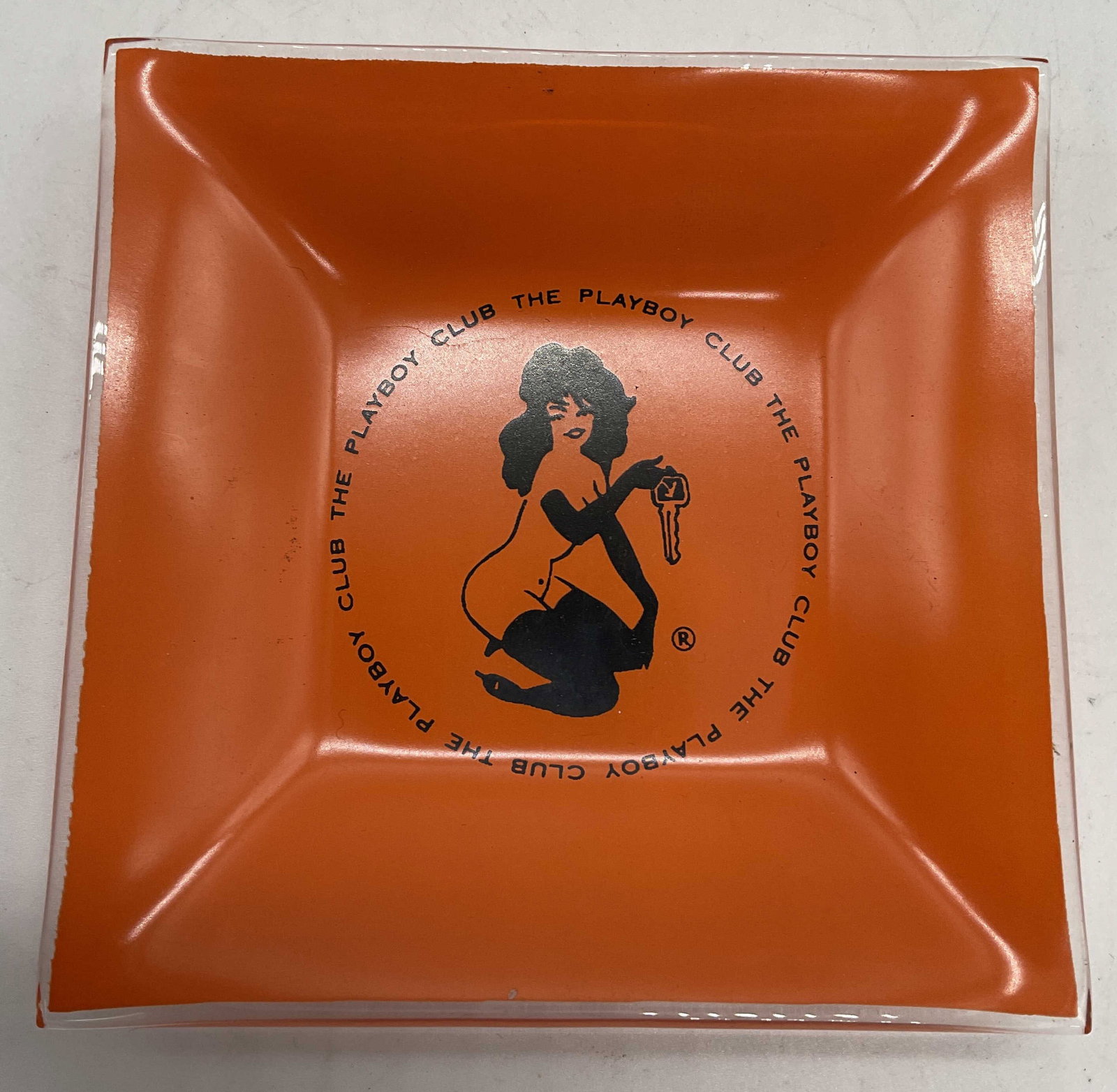 Vintage THE PLAYBOY CLUB Ashtray: Vintage THE PLAYBOY CLUB orange glass Ashtray. Measures approx. 3.5 W in. Some surface wear consistent with age and use. THE PLAYBOY CLUB tabletop decor, decorative arts, THE PLAYBOY CLUB decorative a