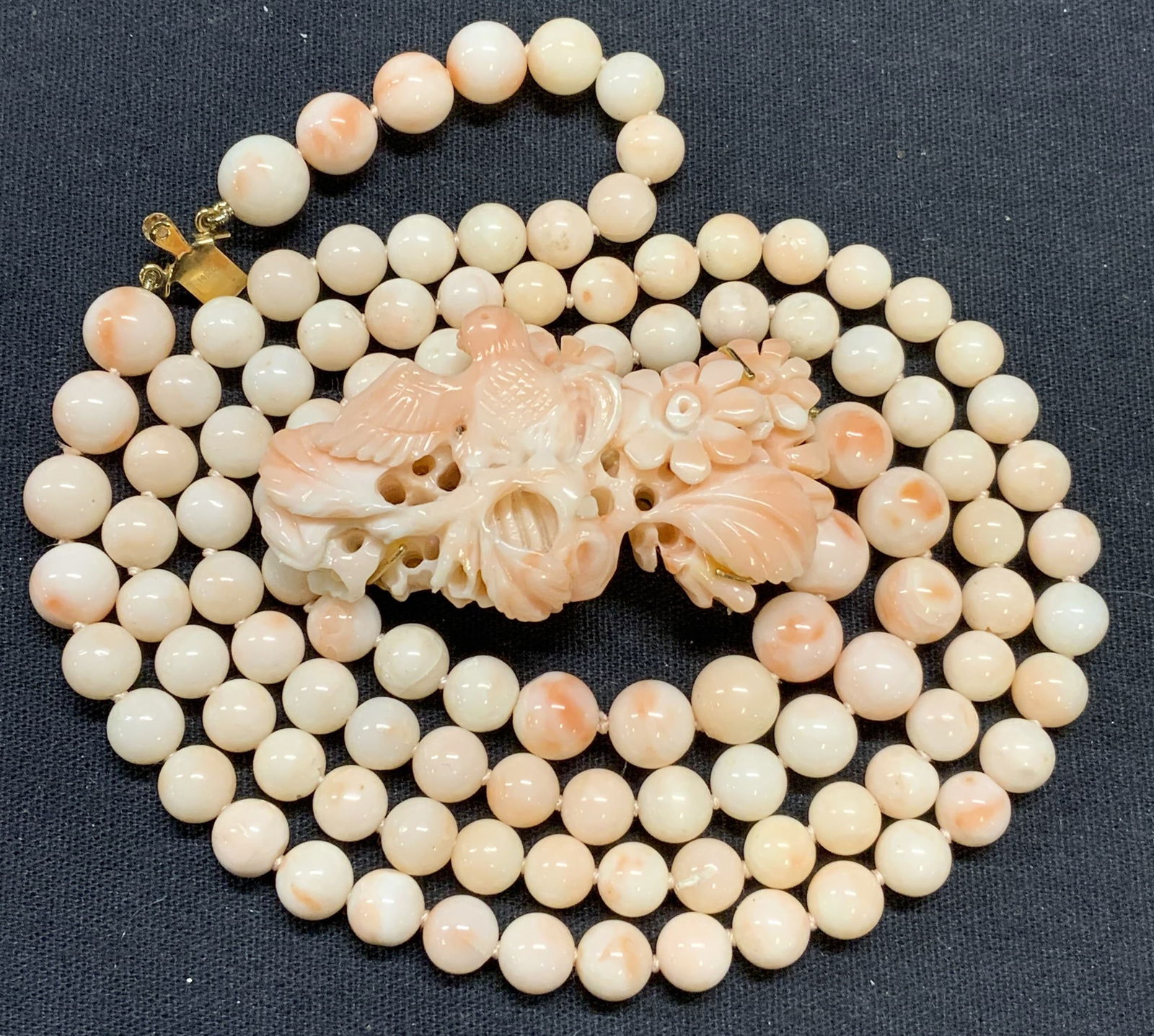 Carved Angel Skin Coral Double Strand Necklace: Vintage double strand angel skin coral beaded necklace on double knotted string with carved bird and flower sculptural clasp. Marked 14K on clasp, makers mark observed on clasp. Some surface wear incl