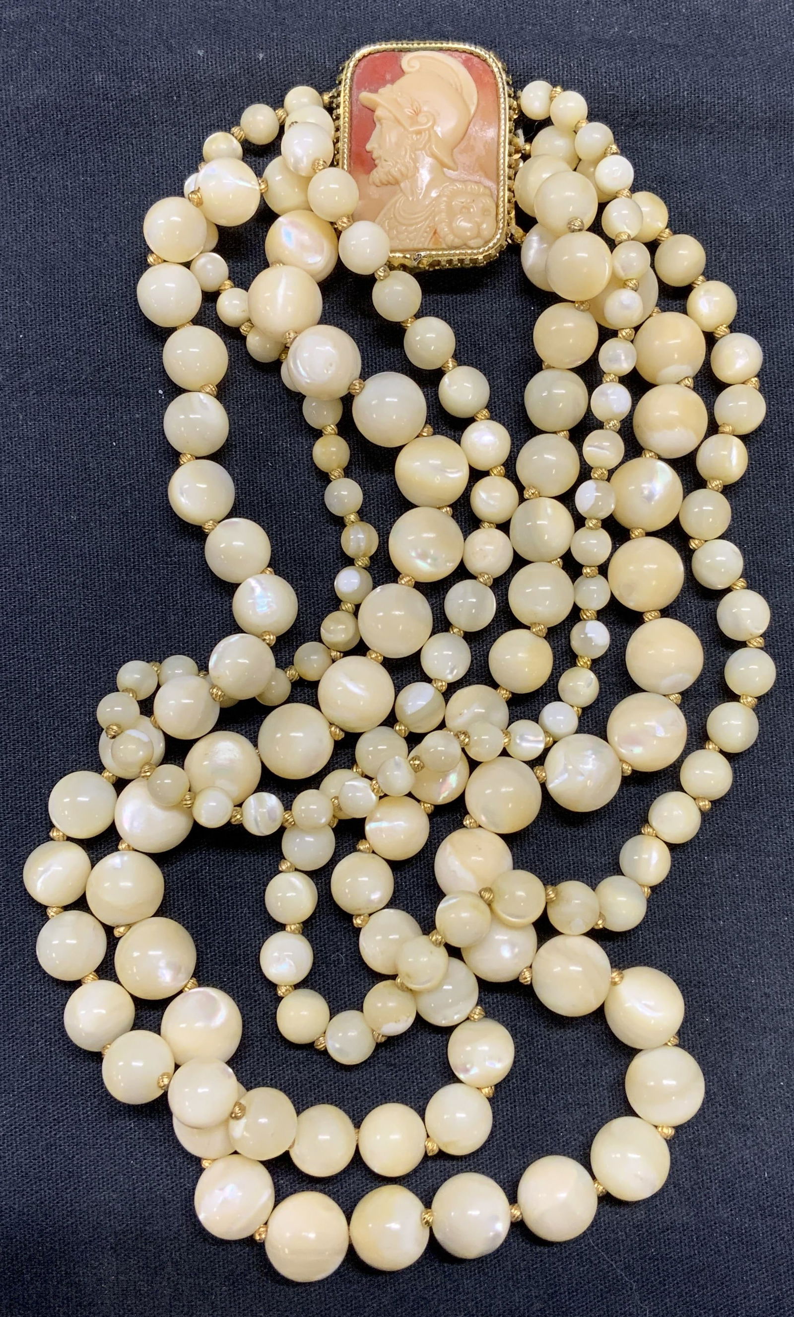 HATTIE CARNEGIE Faux Pearl Cameo Necklace: Vintage Hattie Carnegie glass beaded faux pearl multi strand necklace with carved cameo clasp. Signed to clasp. Drop length of shortest strand approx. 5 inches. Necklace has weight. Some surface wear