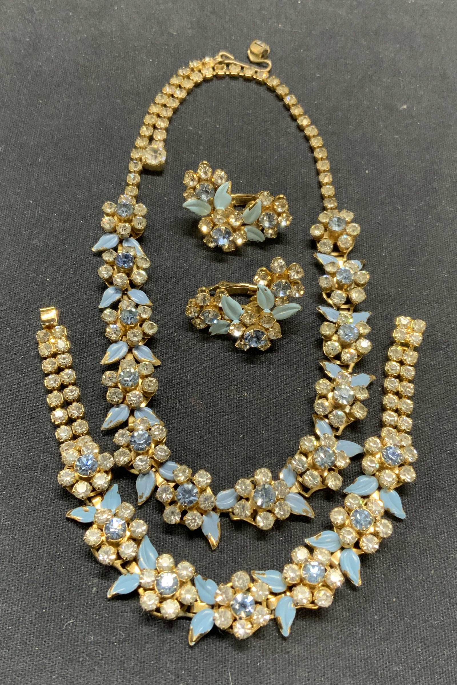 3 Gold Tone Blue Crystal Flower Necklace, More: Lot of 3 jewelry pieces. Vintage matching gold tone colorless and blue crystal decorated necklace, bracelet, and clip on earrings. Necklace drop length approx. 7 inches. Bracelet measures approx. 6.5 