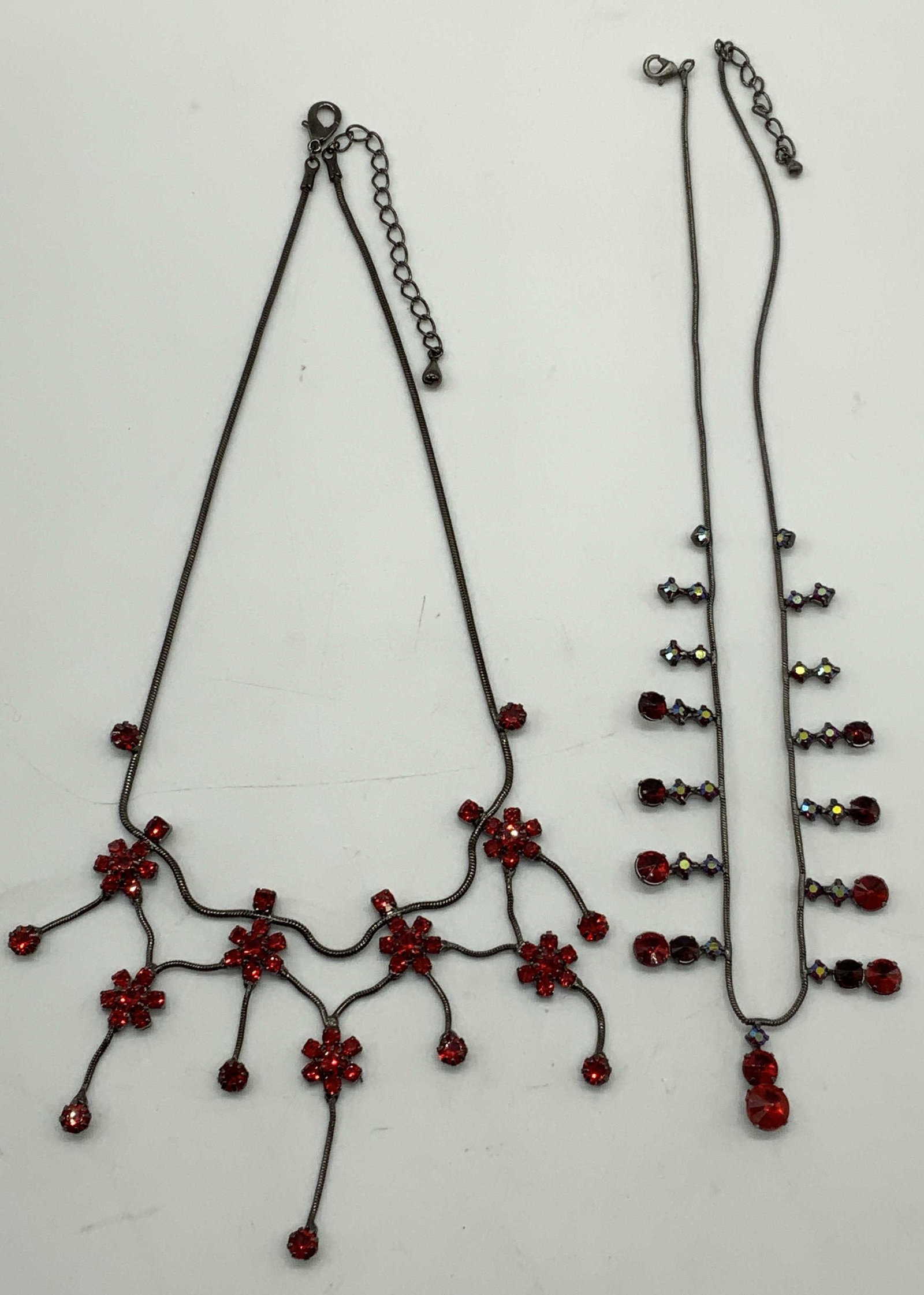 2 Red Crystal Flower Necklace, Pendant Necklace: Lot of 2 jewelry pieces. Black toned necklace with red floral crystal decoration. Drop length approx. 8 inches. Silver toned red crystal pendant necklace. Drop length approx. 8.25 inches. Some surface