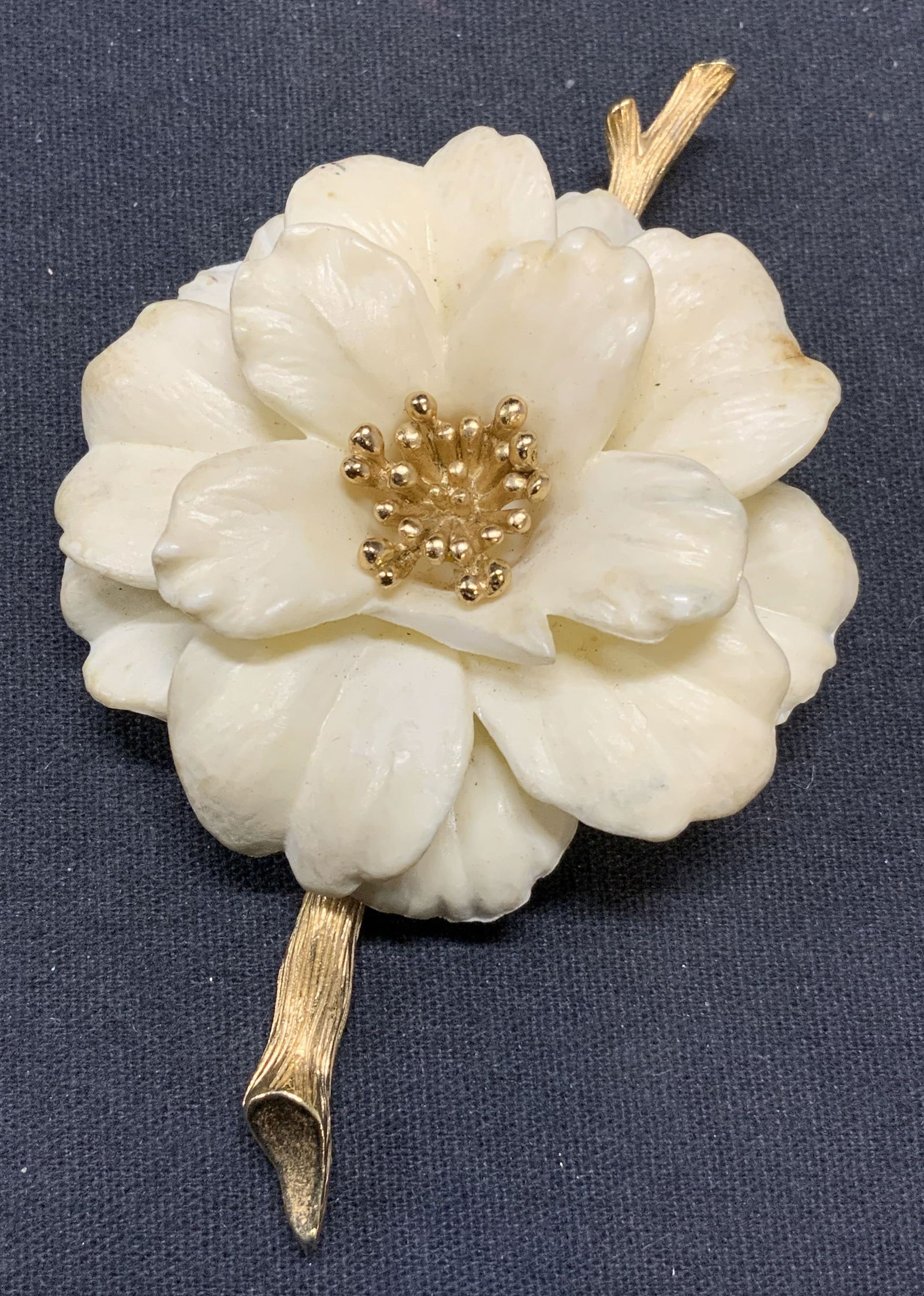 TRIFARI Gold Tone White Flower Brooch: Vintage Trifari gold tone brooch with sculptural white flower. Signed to underside. Hinge pin to underside. Measures approx. 3.25 x 2.25 inches. Some surface wear including scratching and chip to peta