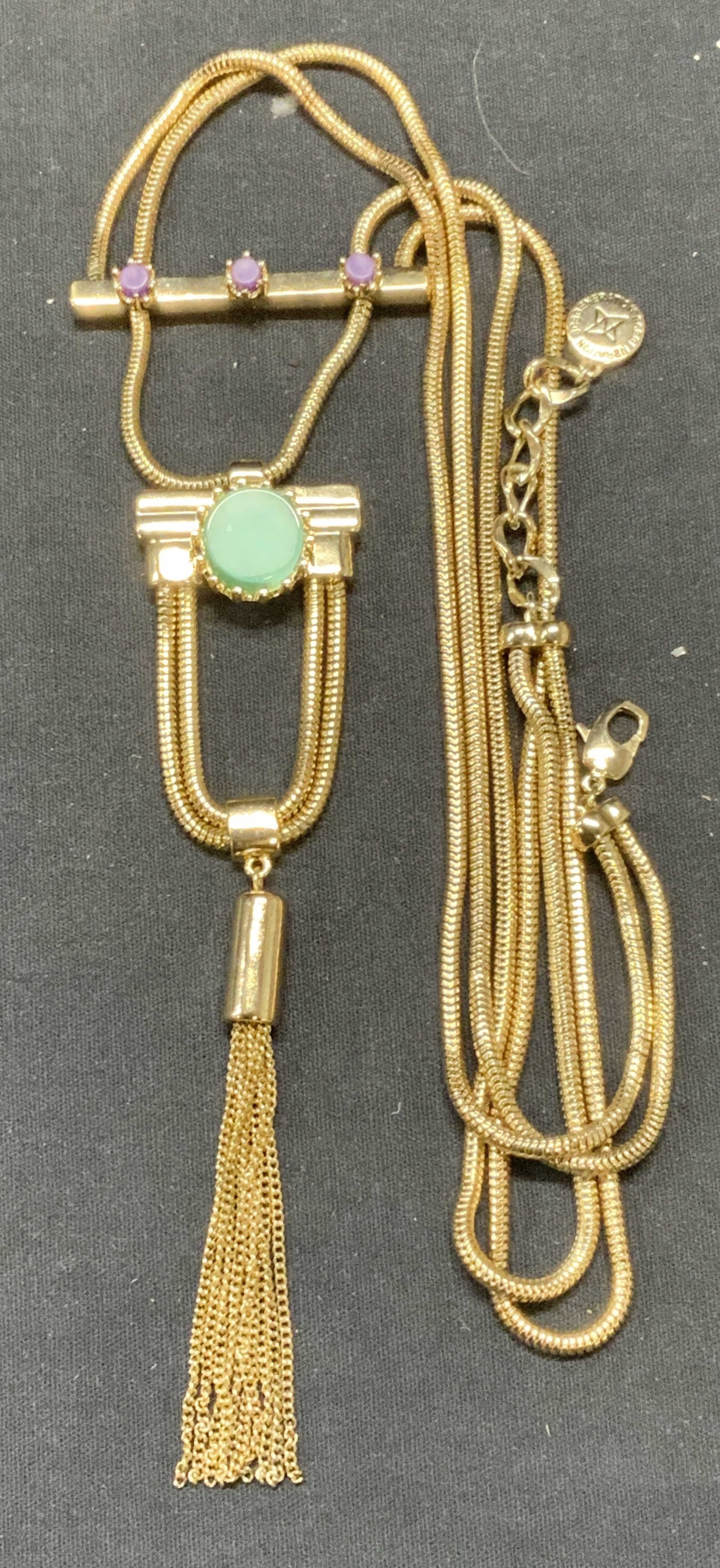 BCBGGENERATION Gold Tone Pendant Necklace: BCBGGENERATION gold tone pendant necklace with purple and green glass cabochons. Signed on hang tag. Drop length 12.5 inches, pendant approx. 7.5 x 2.25 inches. Some surface wear including scratching 