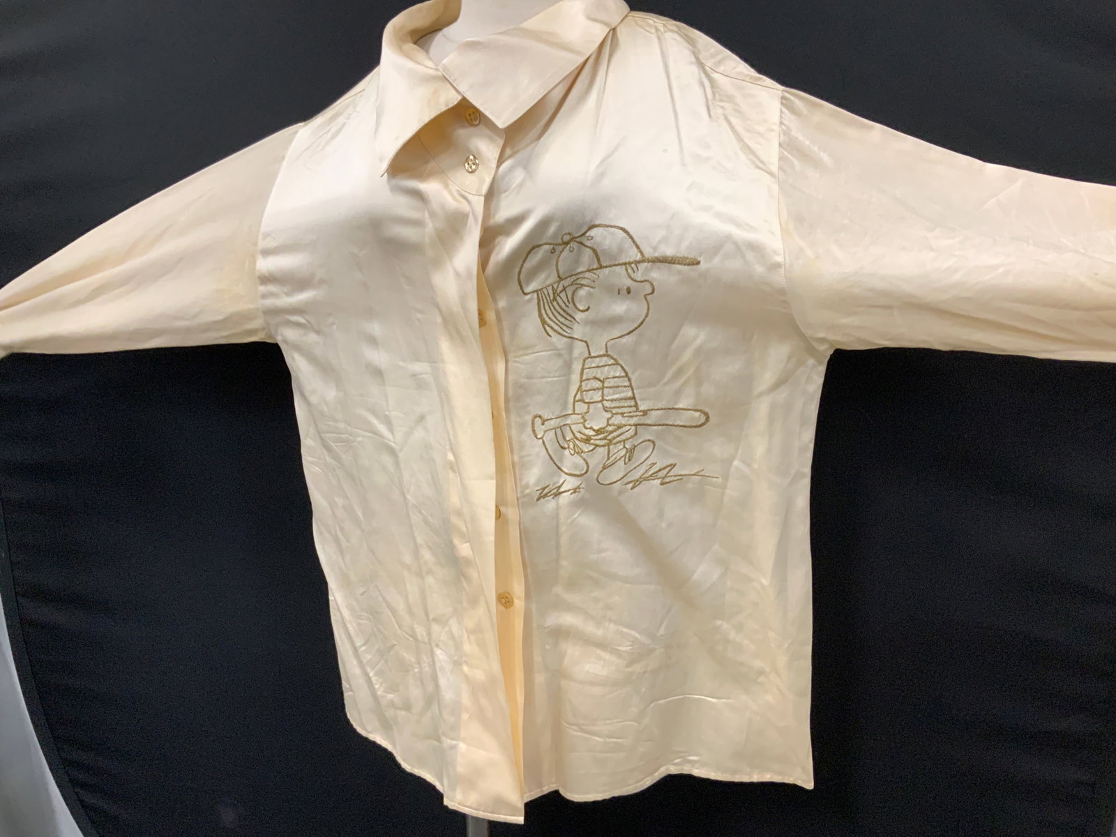 Iceberg Peanuts Character Linus Blouse, Italy: All cotton Cream toned blouse with gold embroidered Linus character from Charles Schultzs The Peanuts. Linus is holding his baseball bat. Exterior is a satiny cotton with a cotton ling. Fold down butt