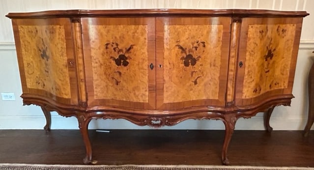 Vintage Continental Inlaid Sideboard: A vintage continental inlaid burl wood sideboard. Inlaid floral and foliage designs. Four doors to the exterior open to reveal storage. One key to interior. Curled legs. Measures approx. 78W x 19.5D x