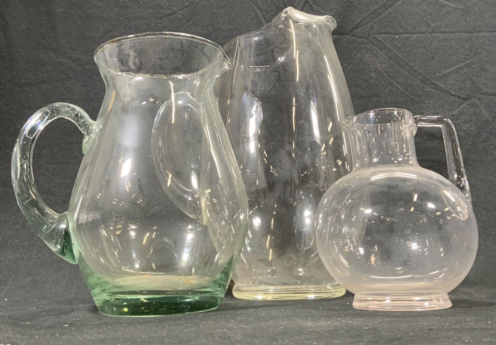 Lot 3 Art Glass Pitchers, Serveware: Lot includes 3 pitchers. Each are glass. Handles of each piece appear to be hand blow/ molded. Largest pitcher measures approximately 10.5 inches tall 8 inches deep 6 inches wide. Pitchers, Glass pitc