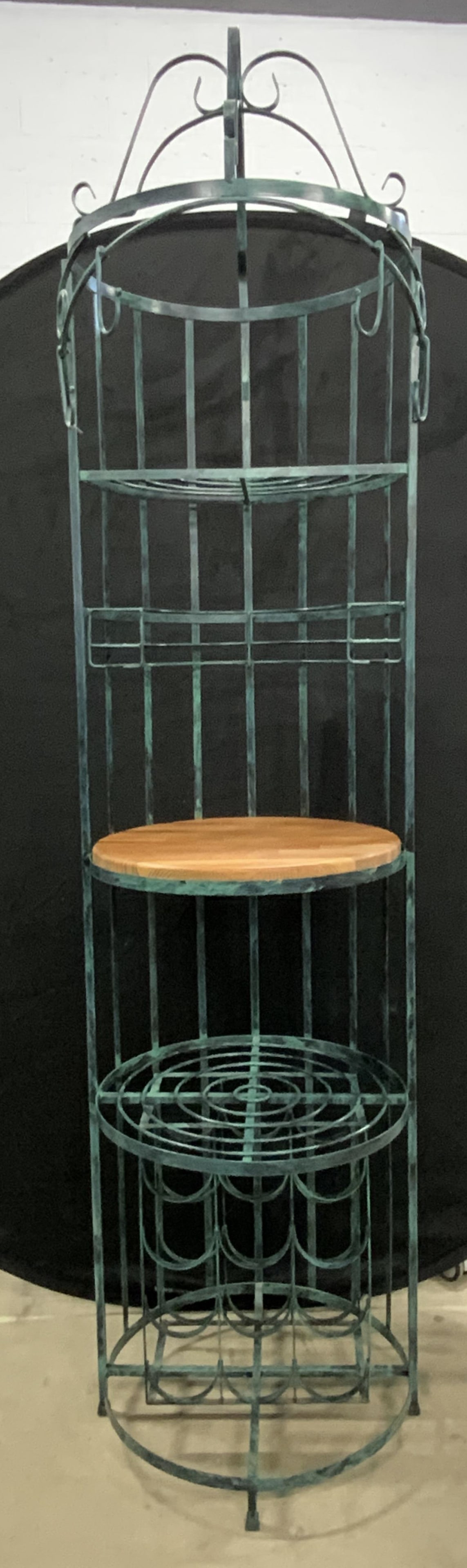 INTERNATIONAL WROUGHT IRON Rustic Iron Wine Rack: A rustic metal, possibly iron, wine rack / bar. Patina style finish. Wooden disc to the center, affixed. Sticker reads INTERNATIONAL WROUGHT IRON. Measures approx. 19D x 19.5W x 79H in. Some wobble to