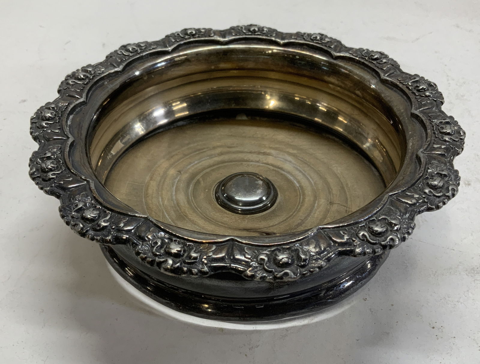 Silver Plate Victorian Wine Bottle Coaster: Silver plate and wood wine/ champagne bottle coaster with scalloped edges and raised Victorian floral decor. No markings. Warped wood , separated from the metal. Possibly antique. 6.75 in. Diameter.2