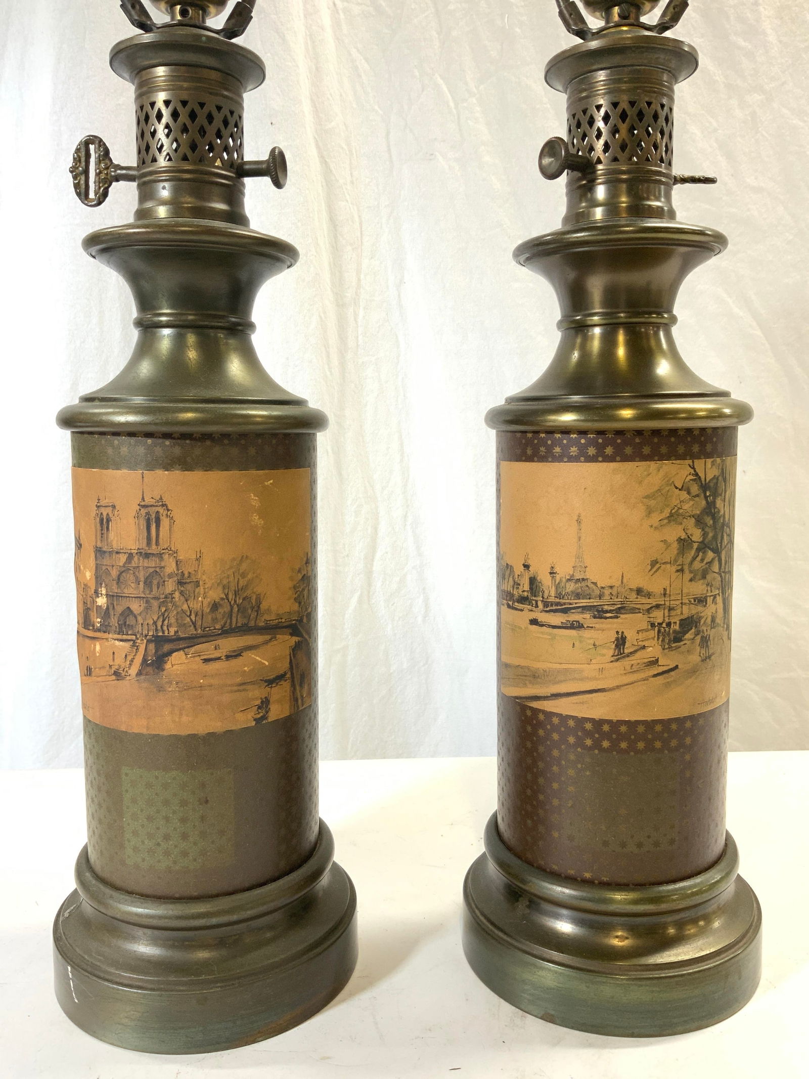 Pair Vntg Tole Lamps W City Scenes: Lot includes 2 lamps. Each are vintage possibly antique. Lamps each have depictions of different city scenes. Lamps each include harps, 1 includes finial. Each lamp has metal base. Height 27 in with f