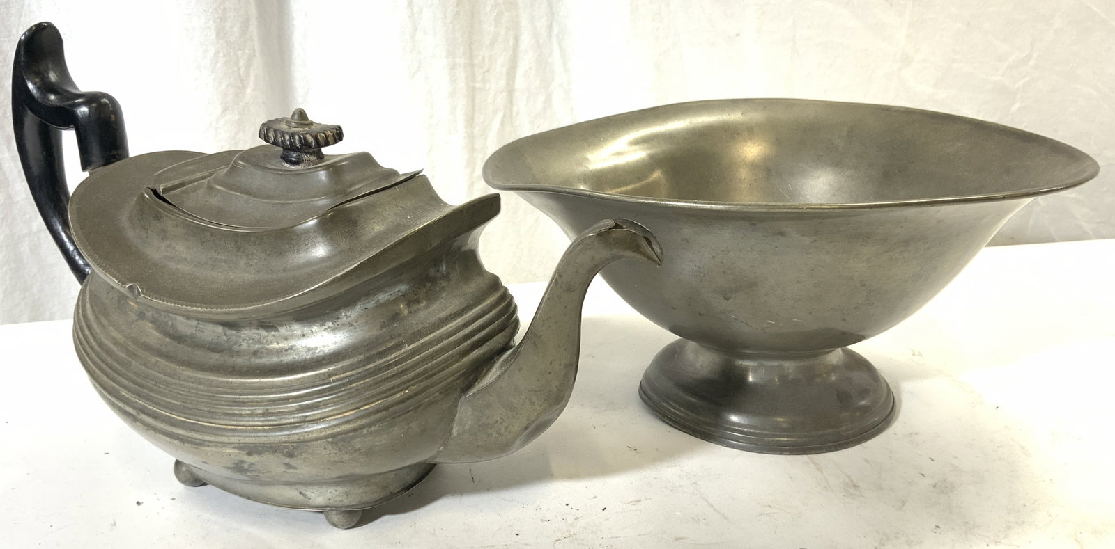 Lot 2 Pewter Footed Teapot & Vessel: Each piece Trademarked illegibly on underside. Lot includes 1 footed teapot & 1 footed bowl. Teapot is lidded with black toned wooden handle. Each piece is pewter. Bowl measures approx 10 inches diame
