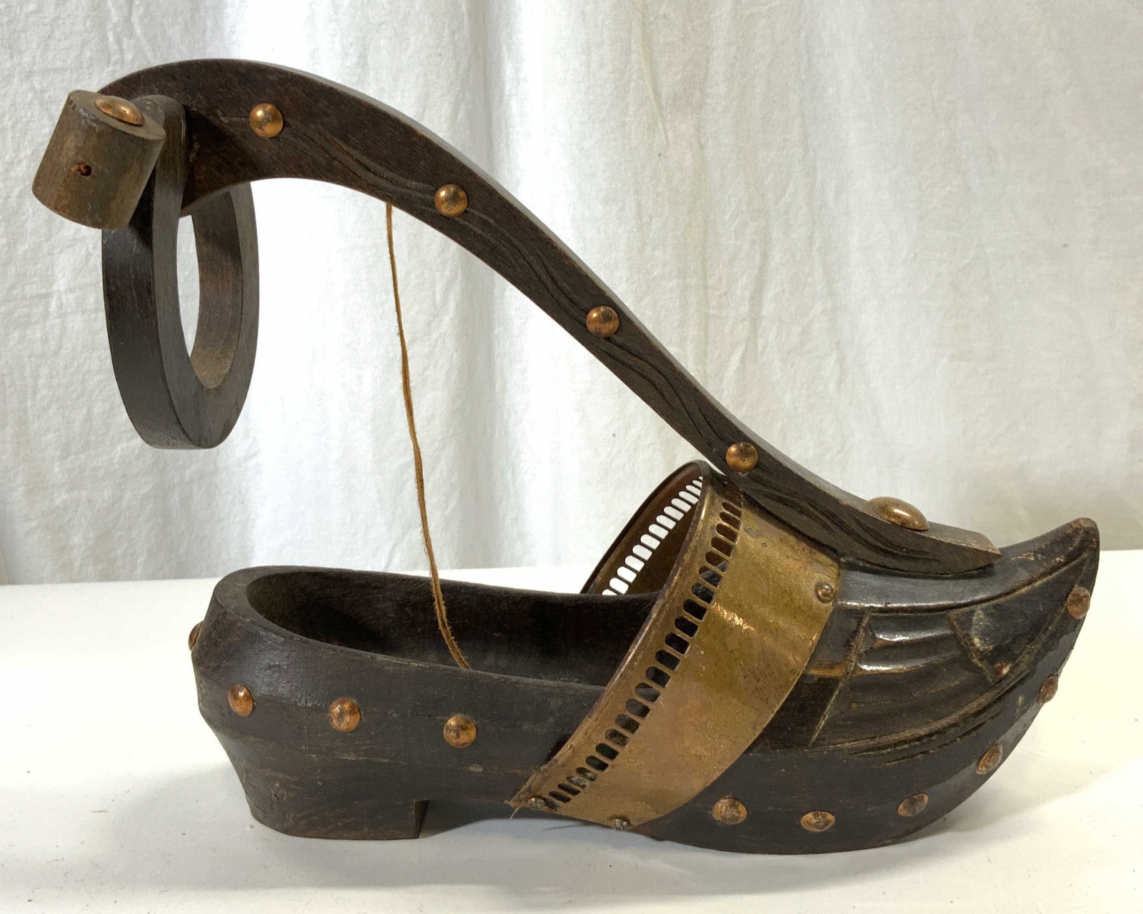 Vintage Carved Wooden Clog Bottle Holder: Bottle Holder is vintage and wooden. Piece is brown toned with studded detail. Bottle Holder has clog shape. Opening has copper toned metal area with pierced detail. Piece measures approximately 9.25 