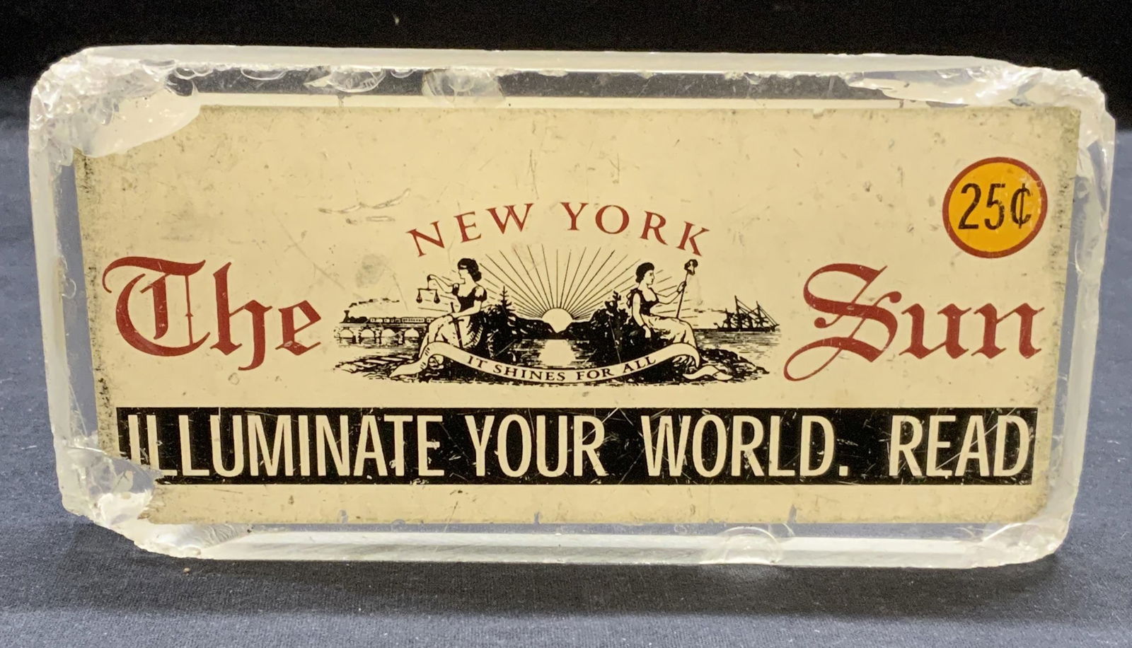 The New York Sun Newspaper Advert Display: The New York Sun vintage lucite newspaper advertisement display. Measures approx. 7.75 x 7/8 x 3.75 inches. Surface wear including chipping and scratching observed. Property of Manhattan estates and f
