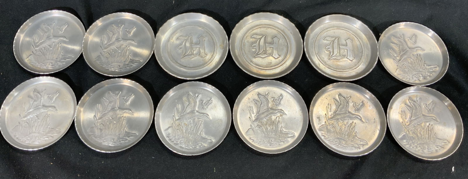 Set 12 Vintage Brushed Metal Coasters: Lot includes 12 coasters. Each are silver toned brushed metal. Three coasters have letter H, 9 have flying bird detail. Each measures approx 3.25 inches wide. Coasters, metal coasters, vintage coaster