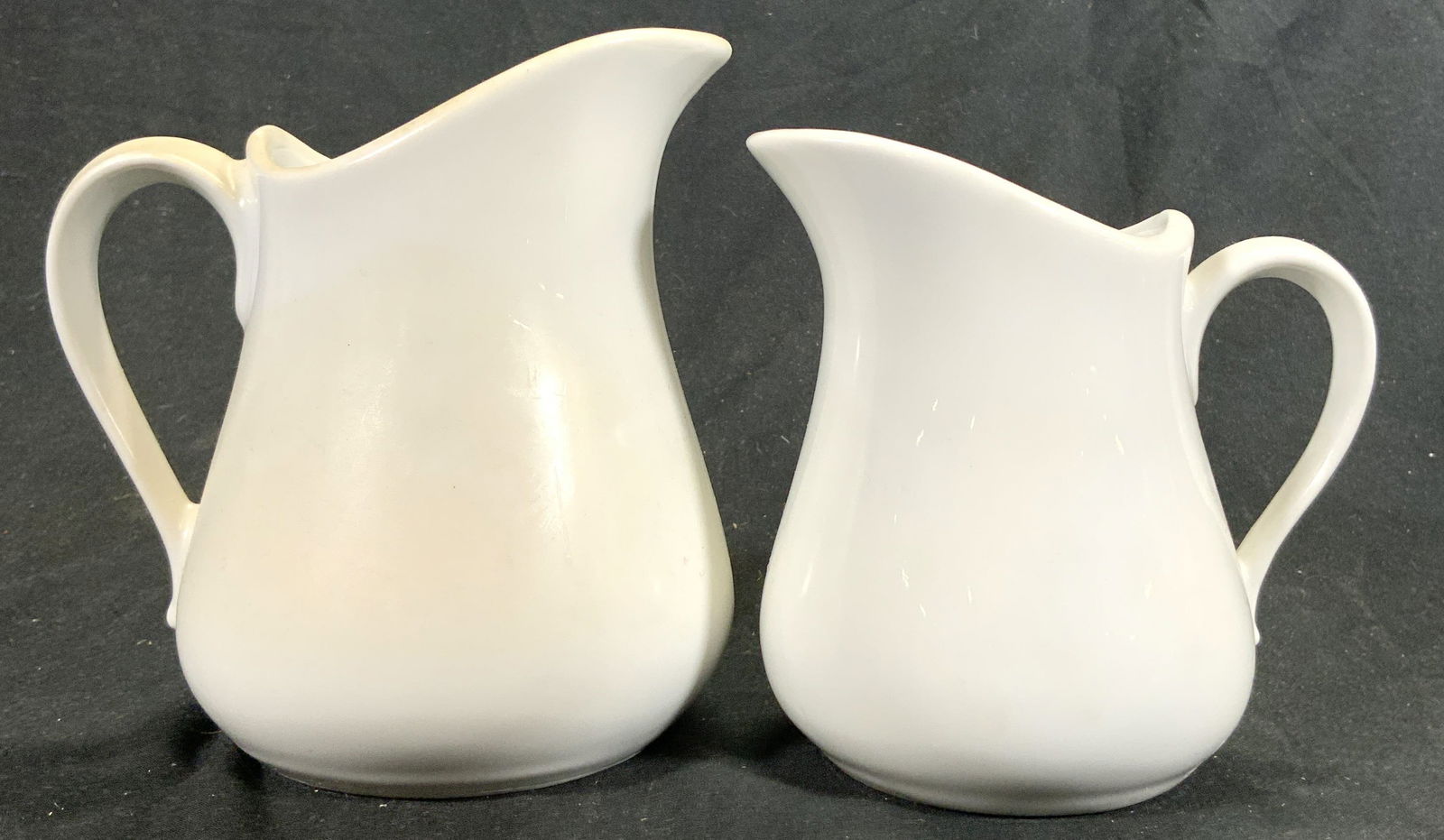 APLICO Lot 2 Porcelain Creamer Dishes FRANCE: Underside are marked APLICO FRANCE. Each piece is white toned and porcelain. Vessels each have half heart shaped handles. Largest creamer dish in lot measures approximately 5.25 inches tall & deep.4 i