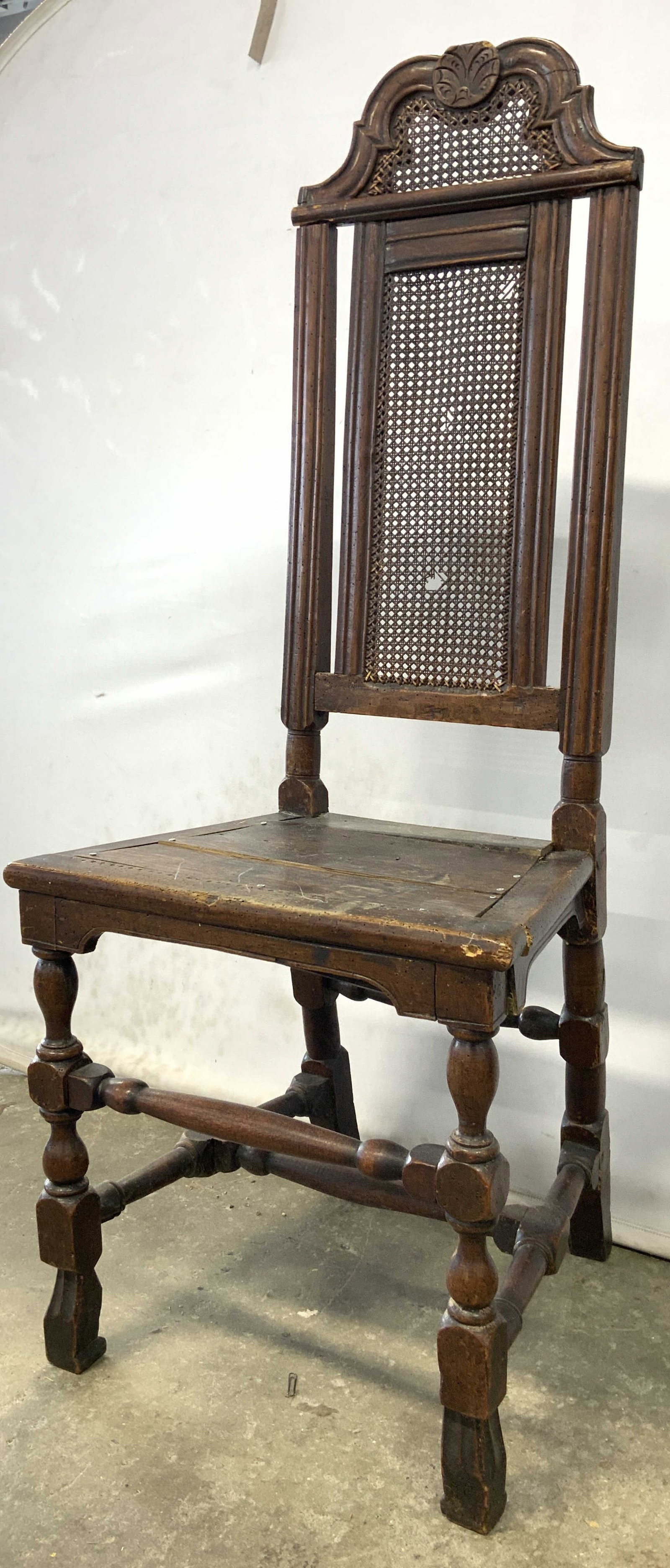 Antique William & Mary Style Wooden Hall Chair: Chair is vintage possibly antique. Piece has William and Mary style, carved relief detail to top of backrest, caned backrest, H shaped stretcher in between carved wooden legs. Chair has tall backrest.