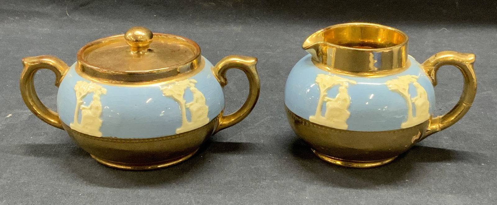 2 Gibsons Gilt Ceramic Cream & Sugar Bowl England: Lot of 2 Gibsons gilt ceramic Wedgwood blue Grecian figural sugar bowl and creamer. Trademarked to undersides. Made in England. Sugar bowl measures approx. 4 x 3 inches. Creamer measures approx. 3.5 x