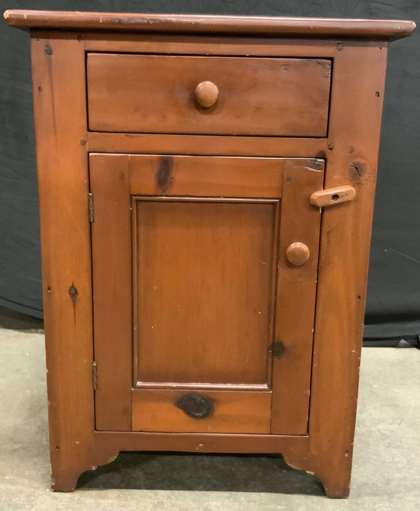 Vintage Wooden Storage Cabinet Nightstand: A vintage wooden storage cabinet nightstand. Brown hued with wood knots present throughout. One drawer and one door to obverse. Door secures closed with a wooden stopper. Dovetailing to the drawer. Me