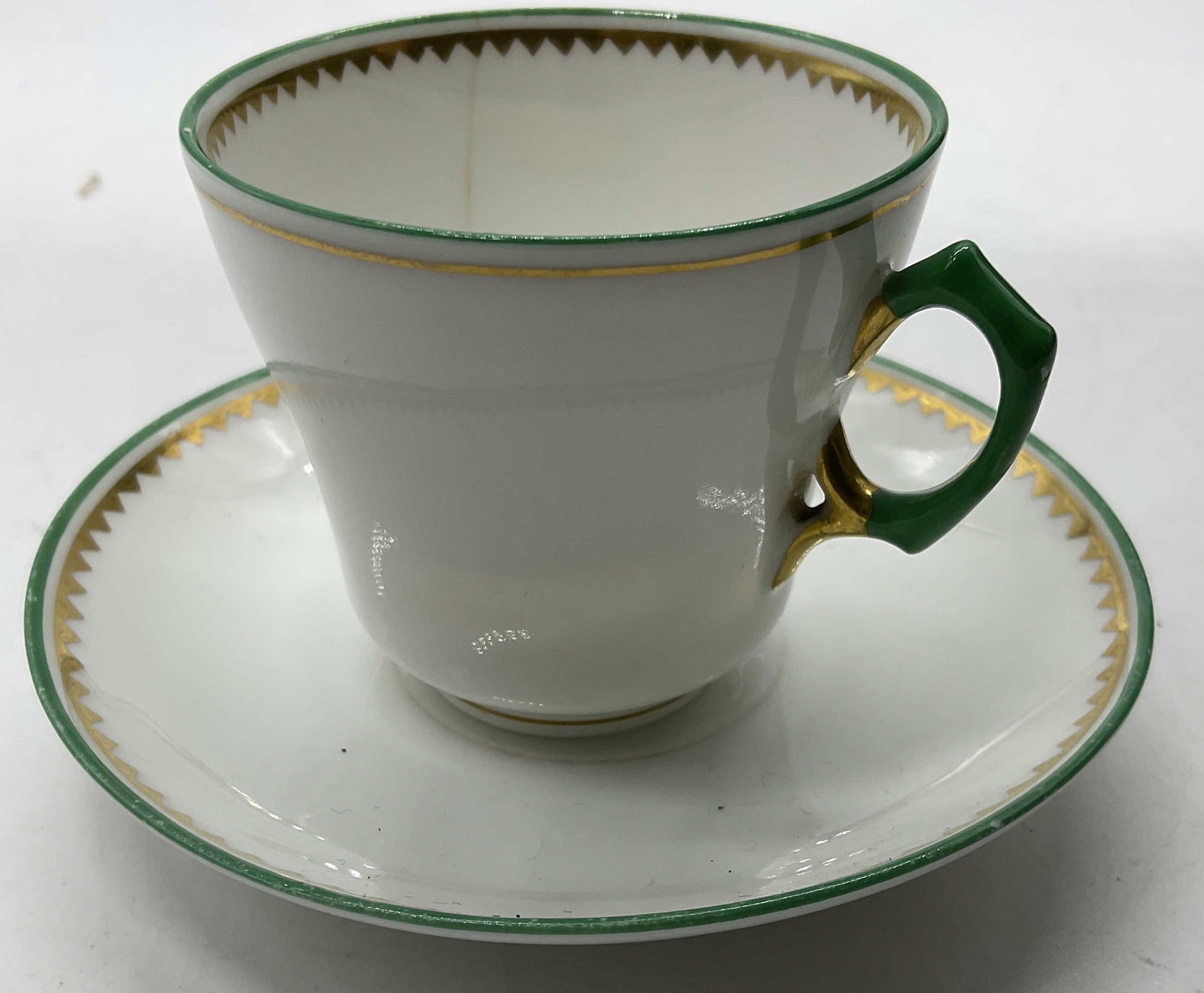Porcelain Demitasse Cup and Saucer: Porcelain Demitasse Cup and Saucer. White with green and gold trim. Some residue present. Saucer measures approx. 4in diameter. Property of Greenwich Connecticut estate. Owners had relocated from thei