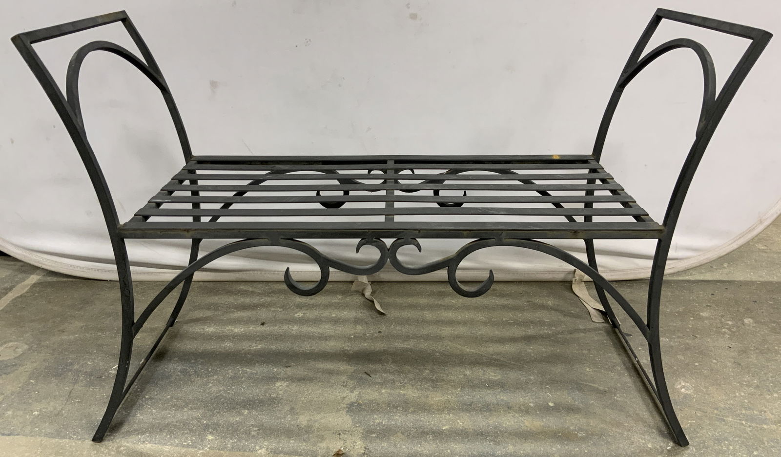 Black Wrought Iron Bench: A wrought iron bench with a black finish. Slat seat with scrollwork designs to the obverse and reverse. Tall curved arms to the sides. Measures approx. 26H x 40W x 16D in. One of two available in this