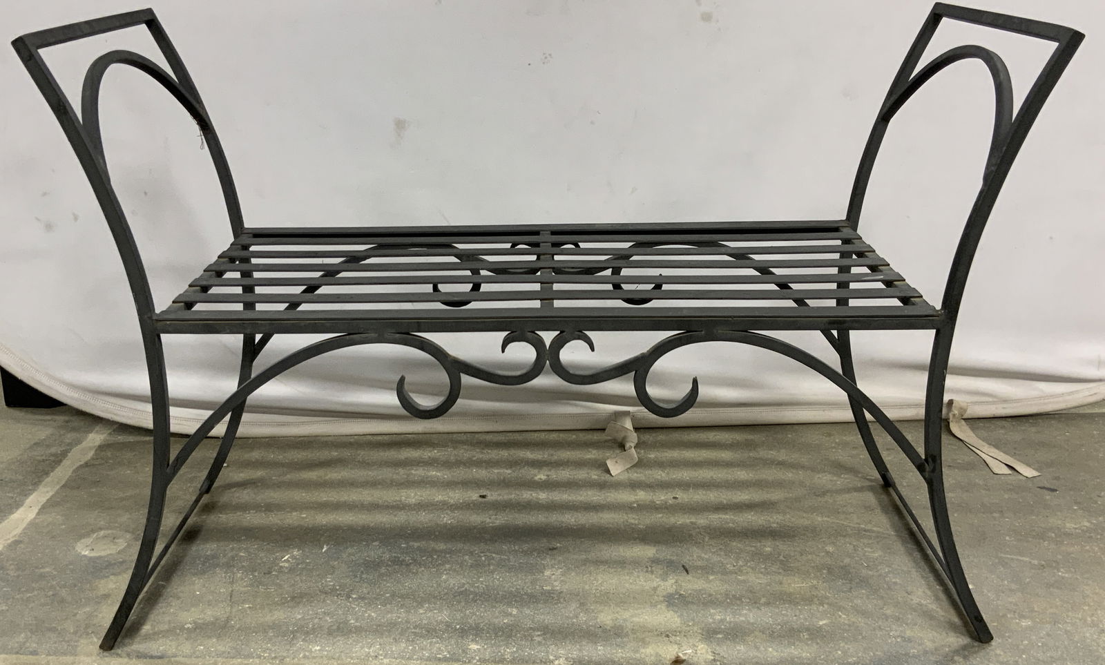 Black Wrought Iron Bench: A wrought iron bench with a black finish. Slat seat with scrollwork designs to the obverse and reverse. Tall curved arms to the sides. Measures approx. 26H x 40W x 16D in. One of two available in this
