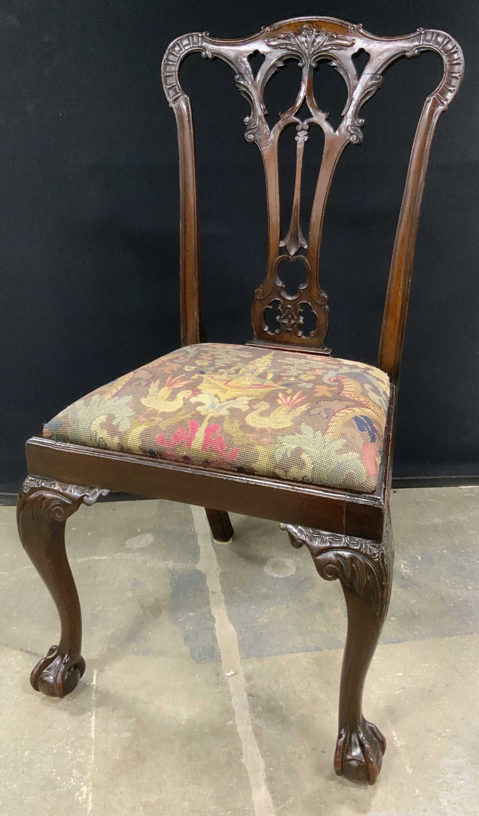 Vintage Chippendale Needlepoint Claw Foot Chair: A vintage Chippendale claw & ball foot chair with a needlepoint seat. The frame of the chair features intricately carved woodwork. The seat features a deity surrounded by birds, florals, and foliage. 