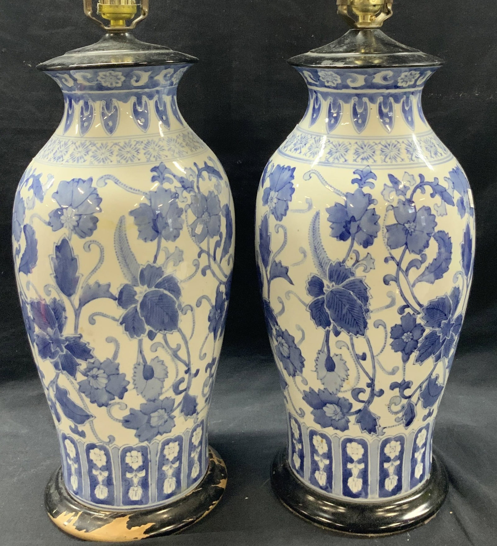 Pr Asian Porcelain Floral Lamps: Pair of white porcelain lamps with blue floral motifs on bodies with black wooden bases and tops and brass harps. Approximately 30 inches tall and 7 inch wide base. Evident loss to paint on wooden bas