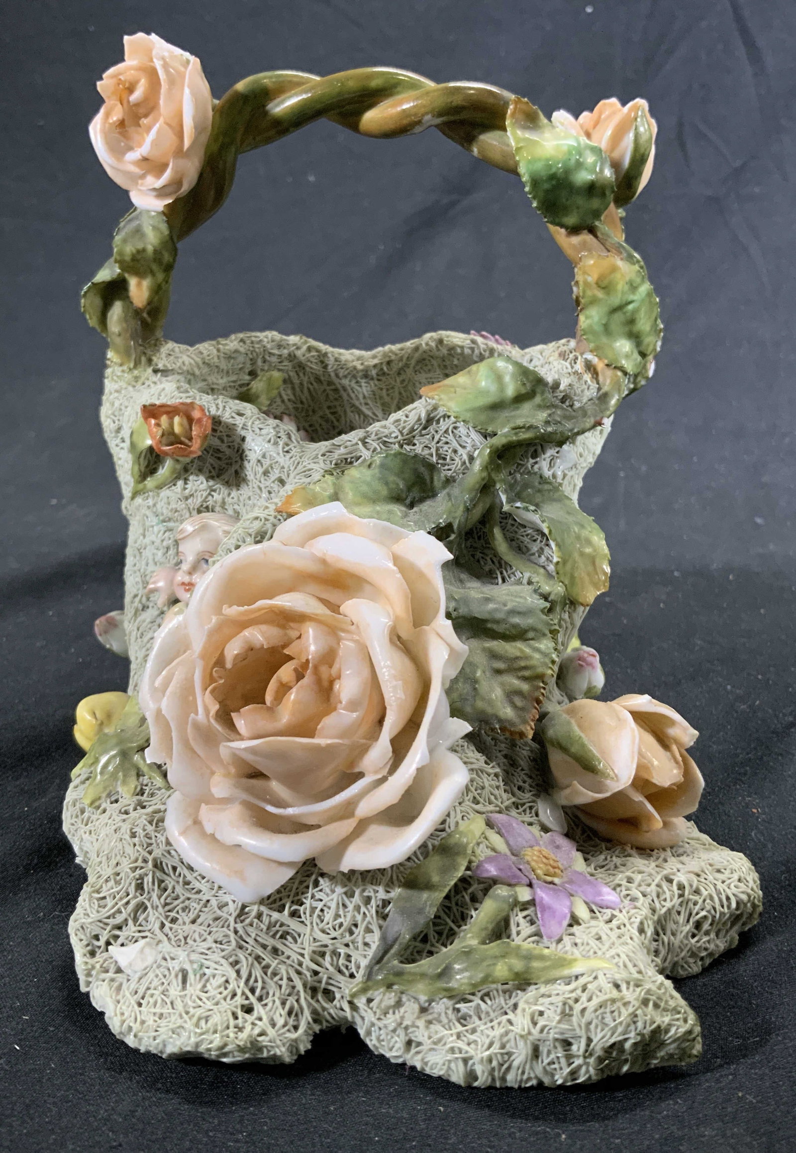 Vintage Woven Floral Porcelain Vessel W Handle: Vessel is vintage and porcelain. Piece has multi toned floral, leaf & baby detail. Top of piece has twisted vine detail. Vessel measures approx 6 inches tall 5 inches wide 7 inches deep. Vessel, porce
