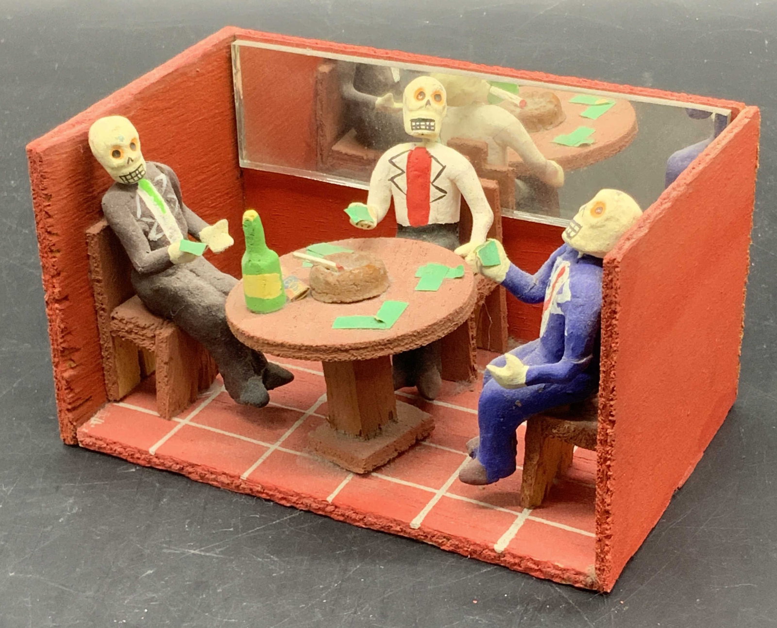 Vintage Handmade Dia de Los Muertos Sculpture, Mx: Vintage Handmade Dia de Los Muertos Sculpture. Piece depicts three skeletons sitting around a table with money, beverages, and cigarettes. Piece appears to be made in Mexico and is crafted from wood,